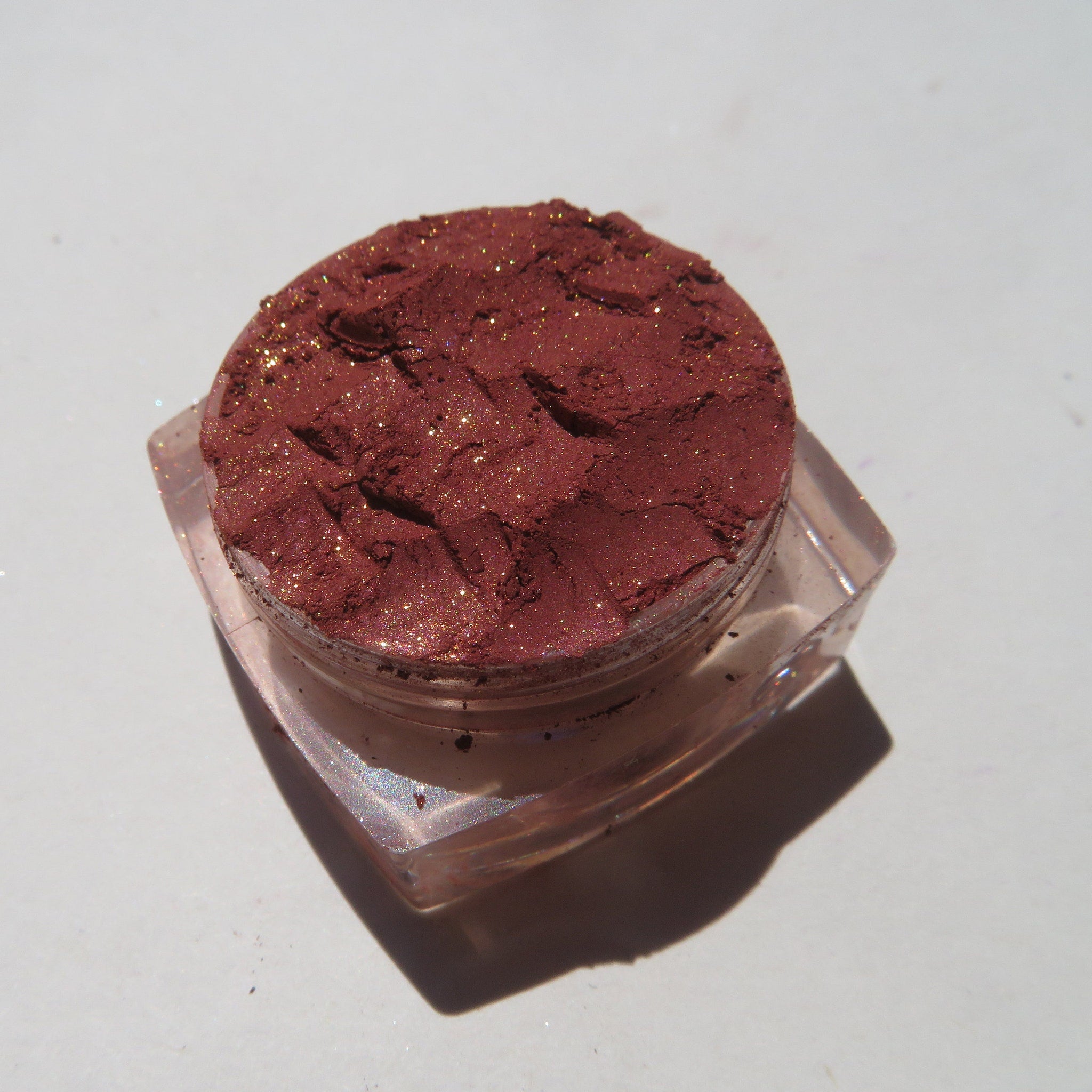 Hand applying brick red orange shimmer loose eyeshadow with fingertip for bold sunset eye look