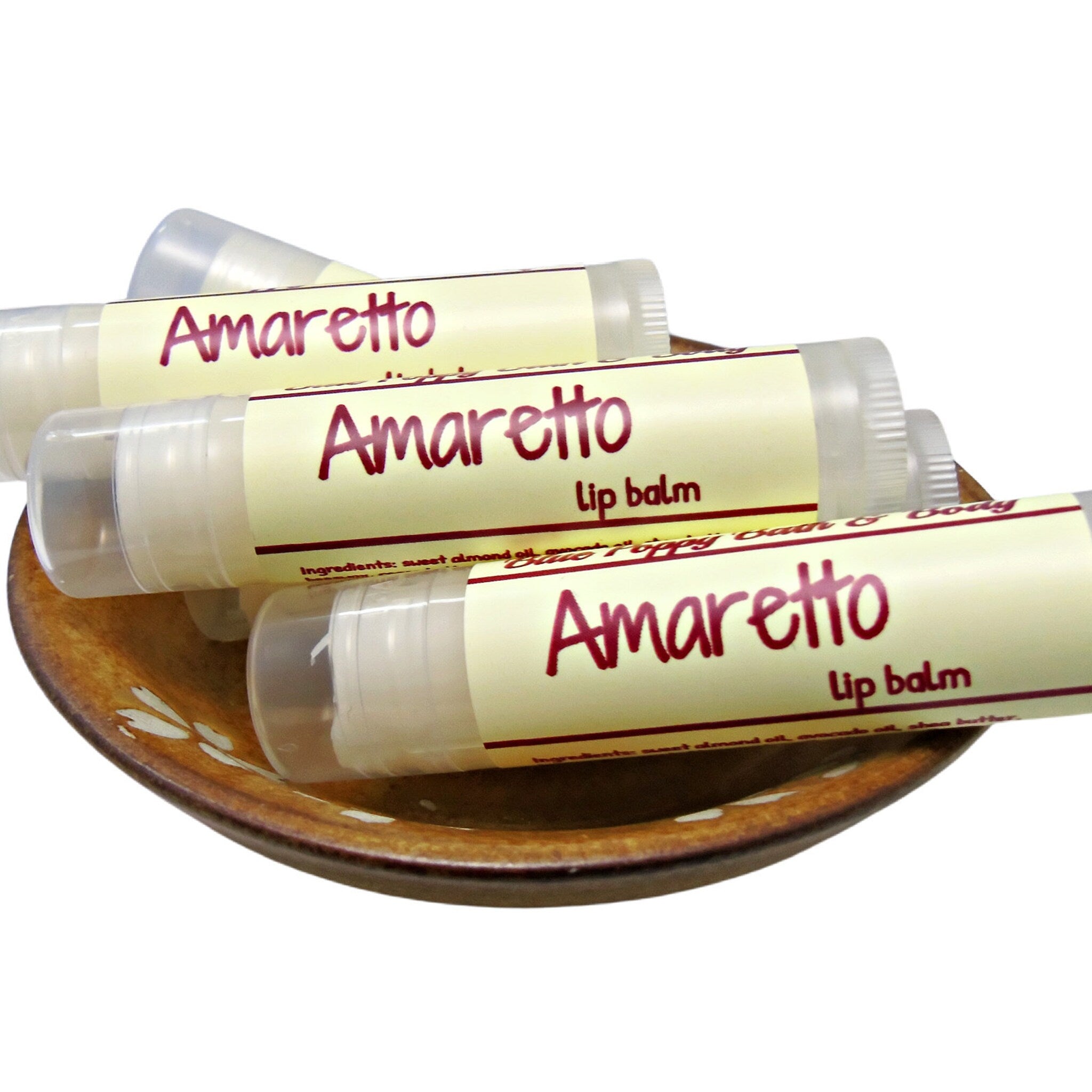 Lip balm tubes with Amaretto label, clear plastic, and beige label on a brown dish