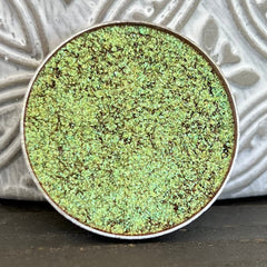 Close-up of holographic multi-chrome eyeshadow pan showing shifting iridescent hues in compact