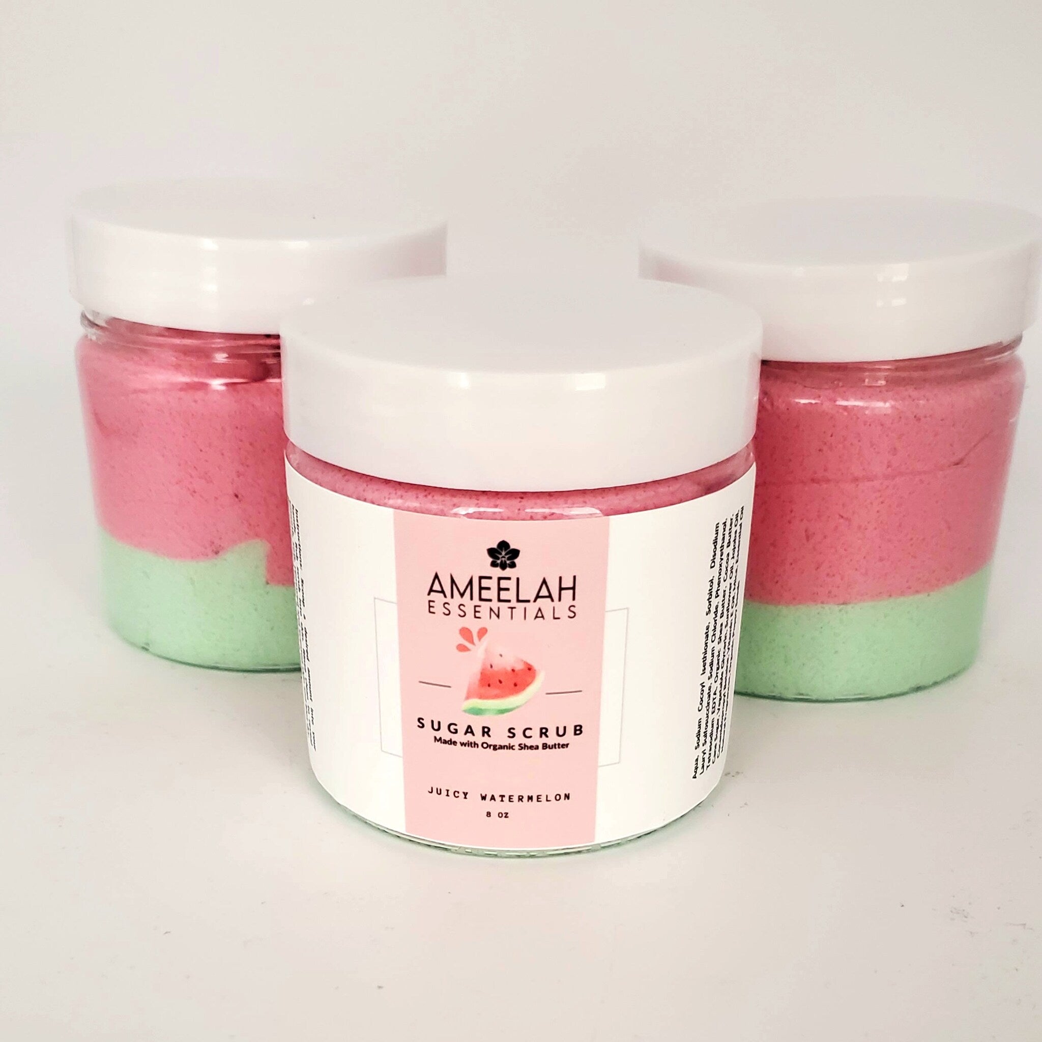 Sugar scrub jars with pink and green layers, white lids, and Ameelah Essentials label