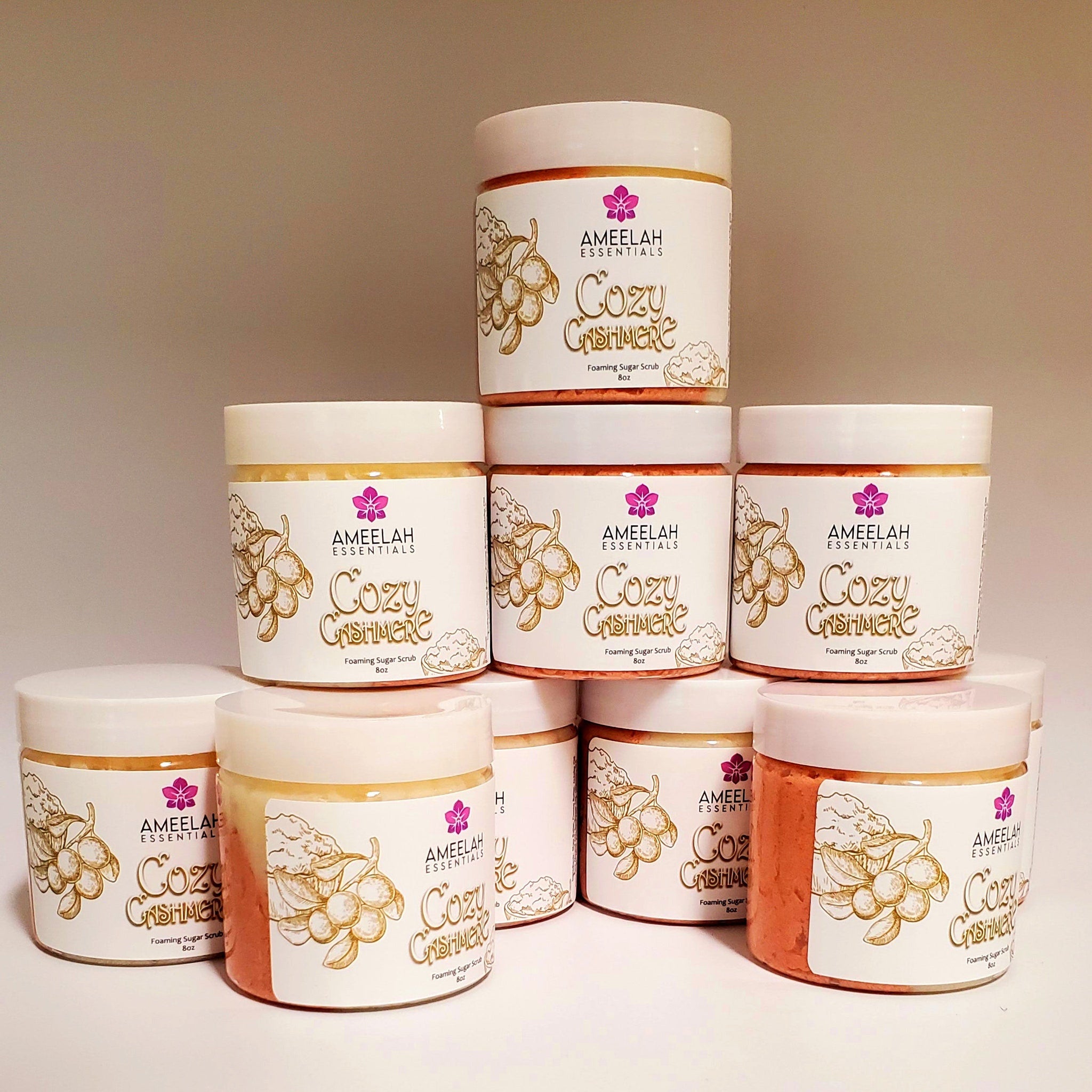 Foaming sugar scrub jars with white lids, labels, and orange/yellow product, Ameelah Essentials branding visible
