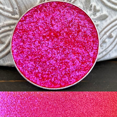 Pressed eyeshadow pan with holographic multi-chrome finish shifting between rosy pink and iridescent hues in compact packaging
