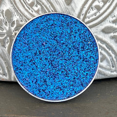 Close-up of multichrome pressed eyeshadow pan shifting between violet, teal, and bronze hues with metallic finish