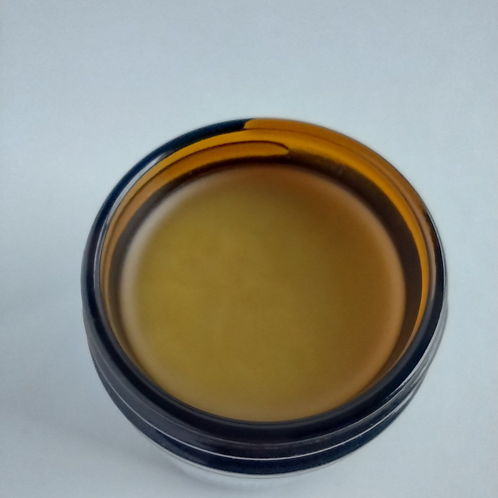 Lip balm jar with yellow balm, brown glass, and black rim detail