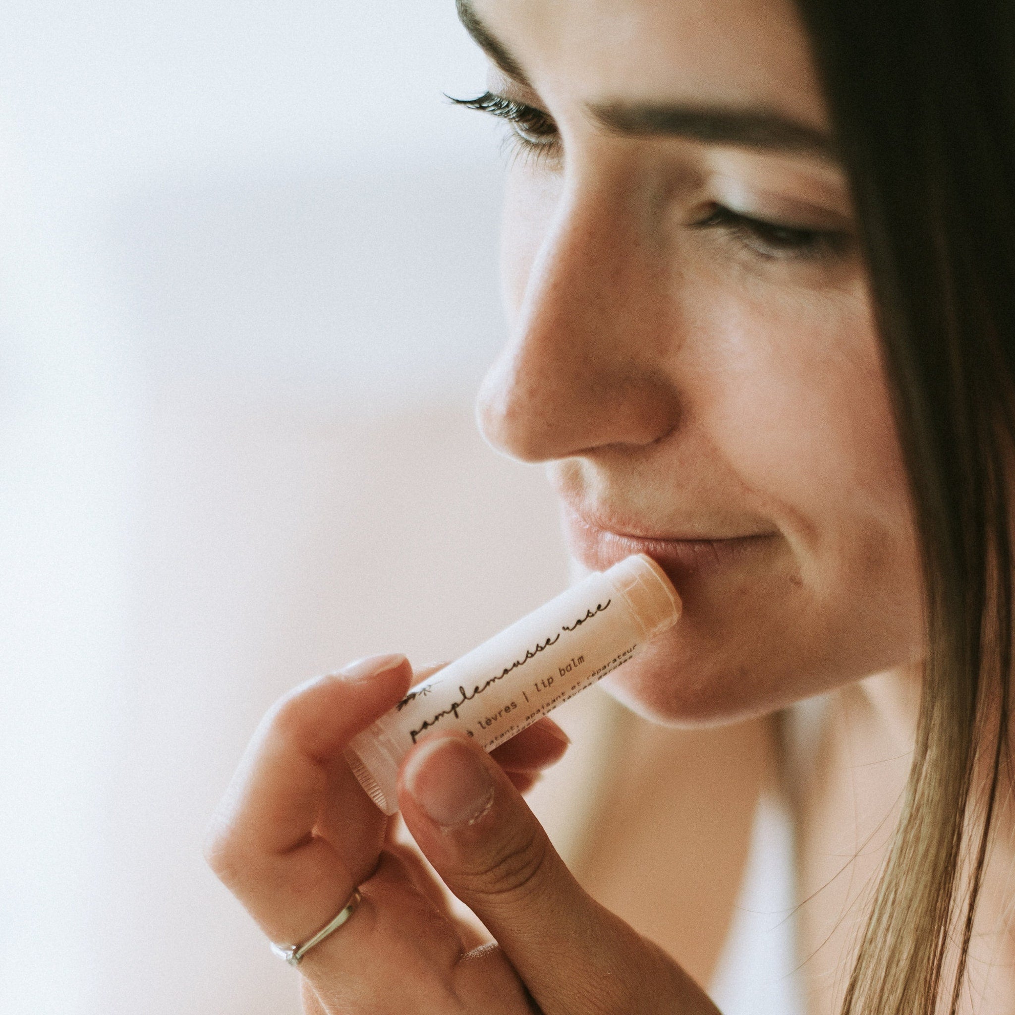 Lip balm tube with white label, light pink color, being applied to lips