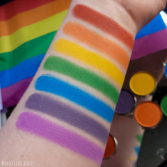 Hand applying vibrant rainbow matte eyeshadow from palette with brush onto eyelid