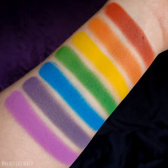 Side view of rainbow pride eyeshadow palette showing seven vibrant matte shades in rectangular pans