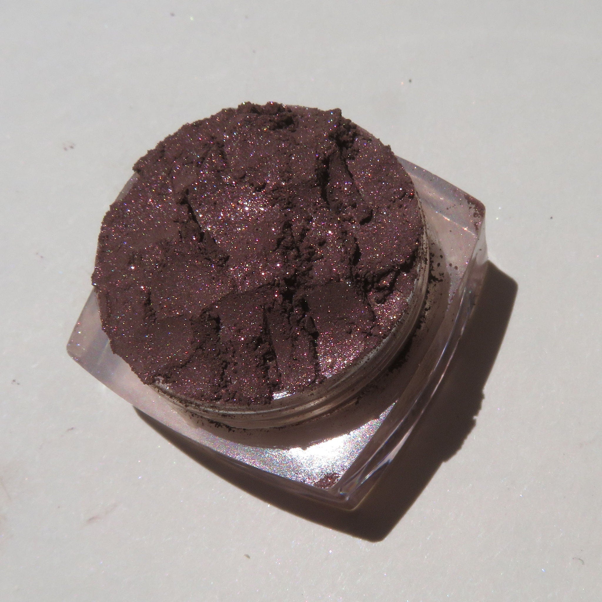 Close-up of dark brown shimmer loose mineral eyeshadow with eco-friendly packaging, showcasing fine sparkle texture