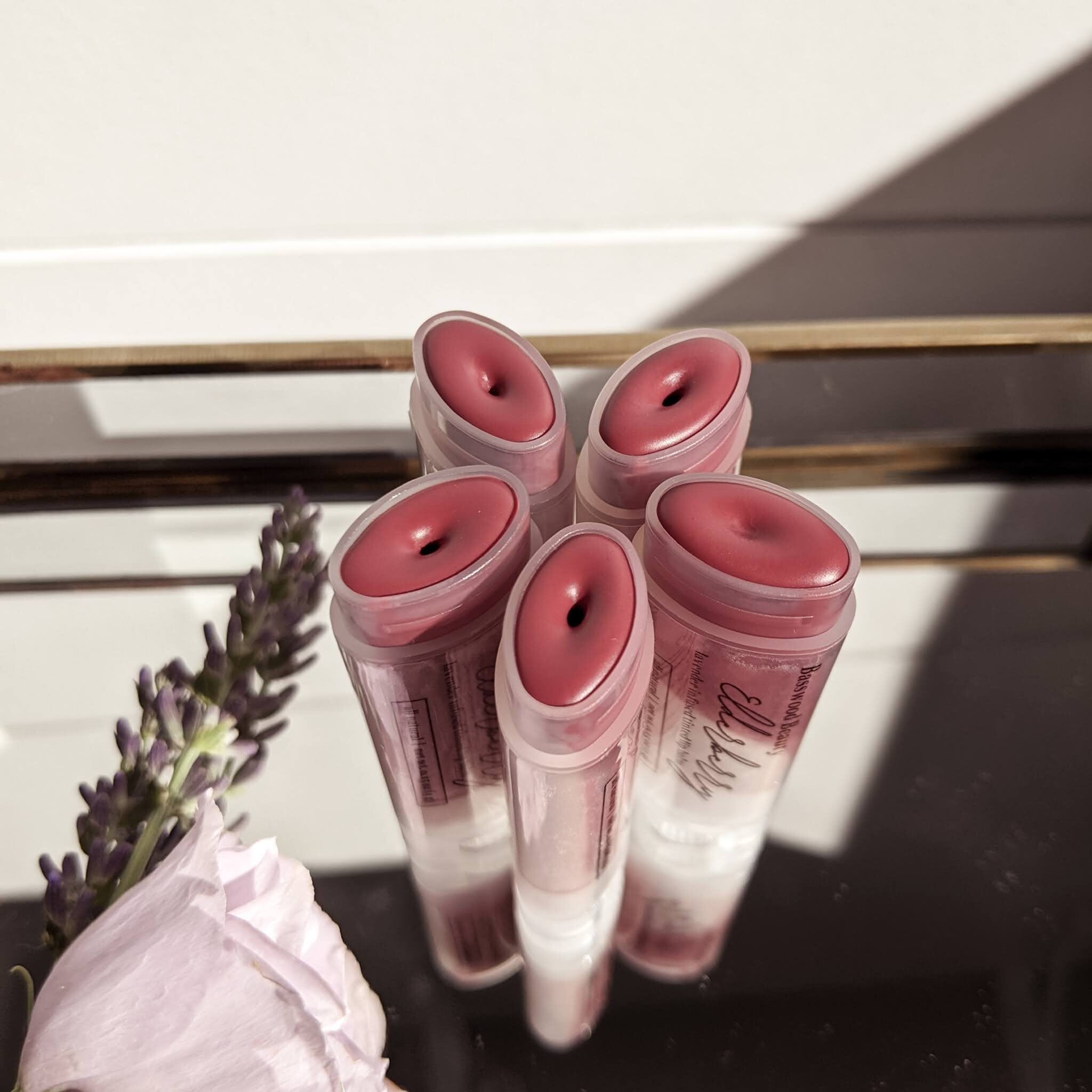 Lip balm tubes with pink tinted balm, clear plastic casing, and Basswood Beauty branding