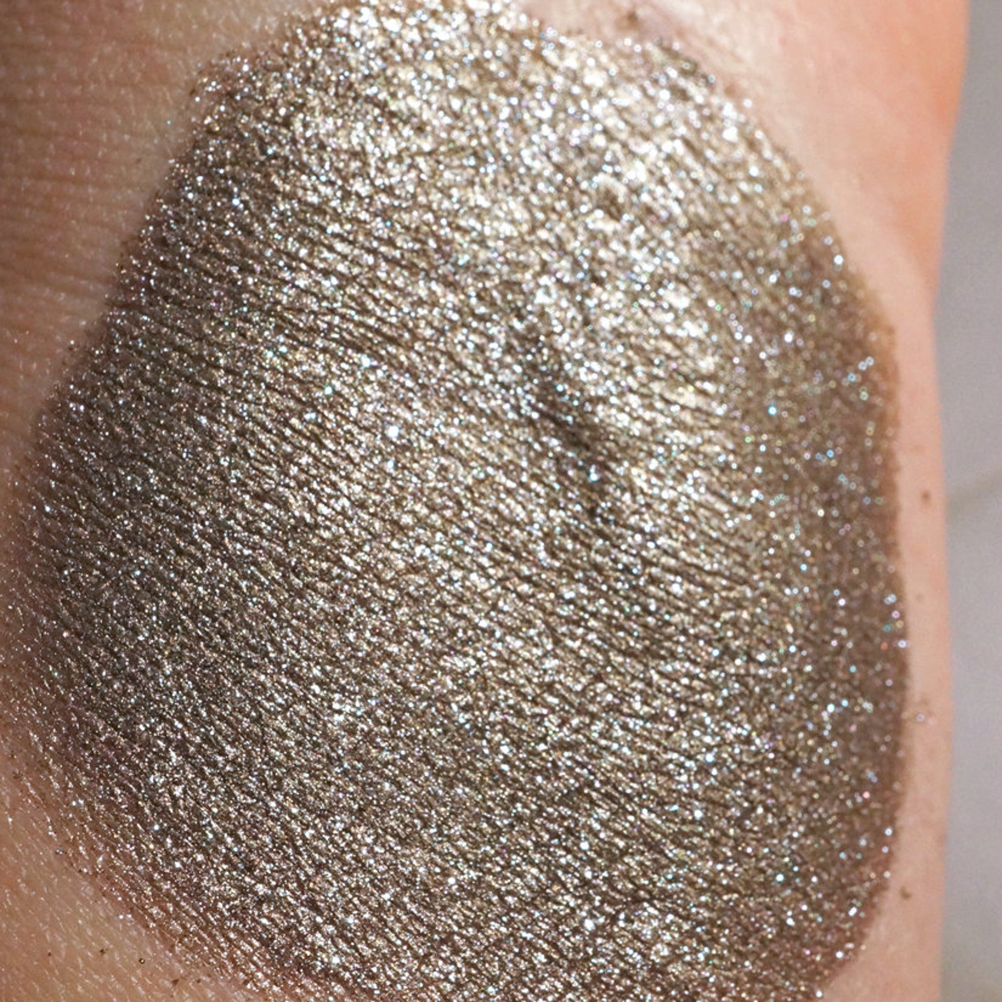 Close-up of loose bronze eyeshadow pigment with silver and blackened gold glitter particles shimmering in light