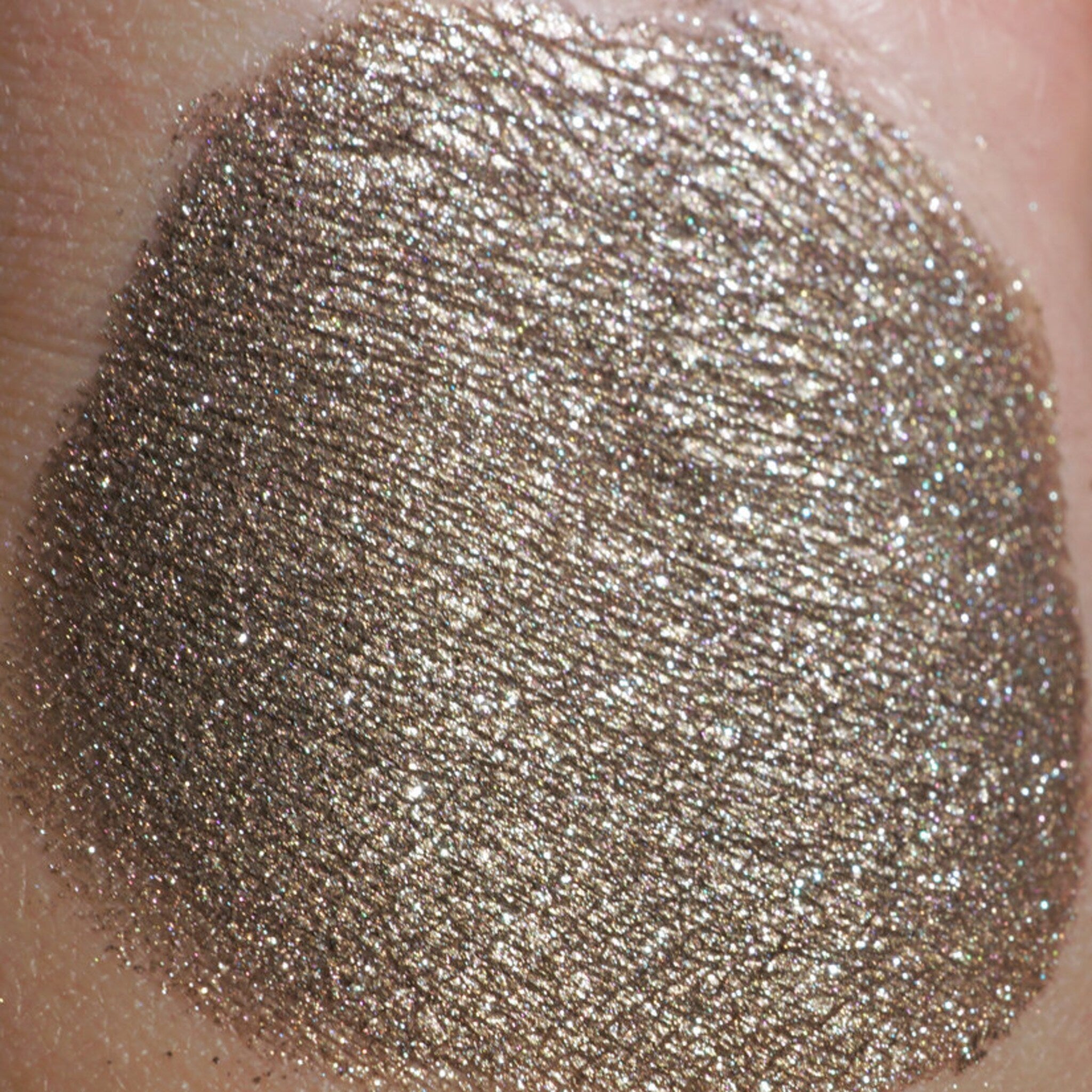 Side view of loose bronze eyeshadow pigment with silver and blackened gold glitter particles catching light