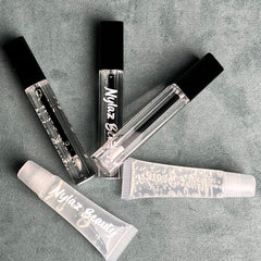 Lip gloss tubes, clear plastic, black caps, with Nylaz Beauty text, on gray surface