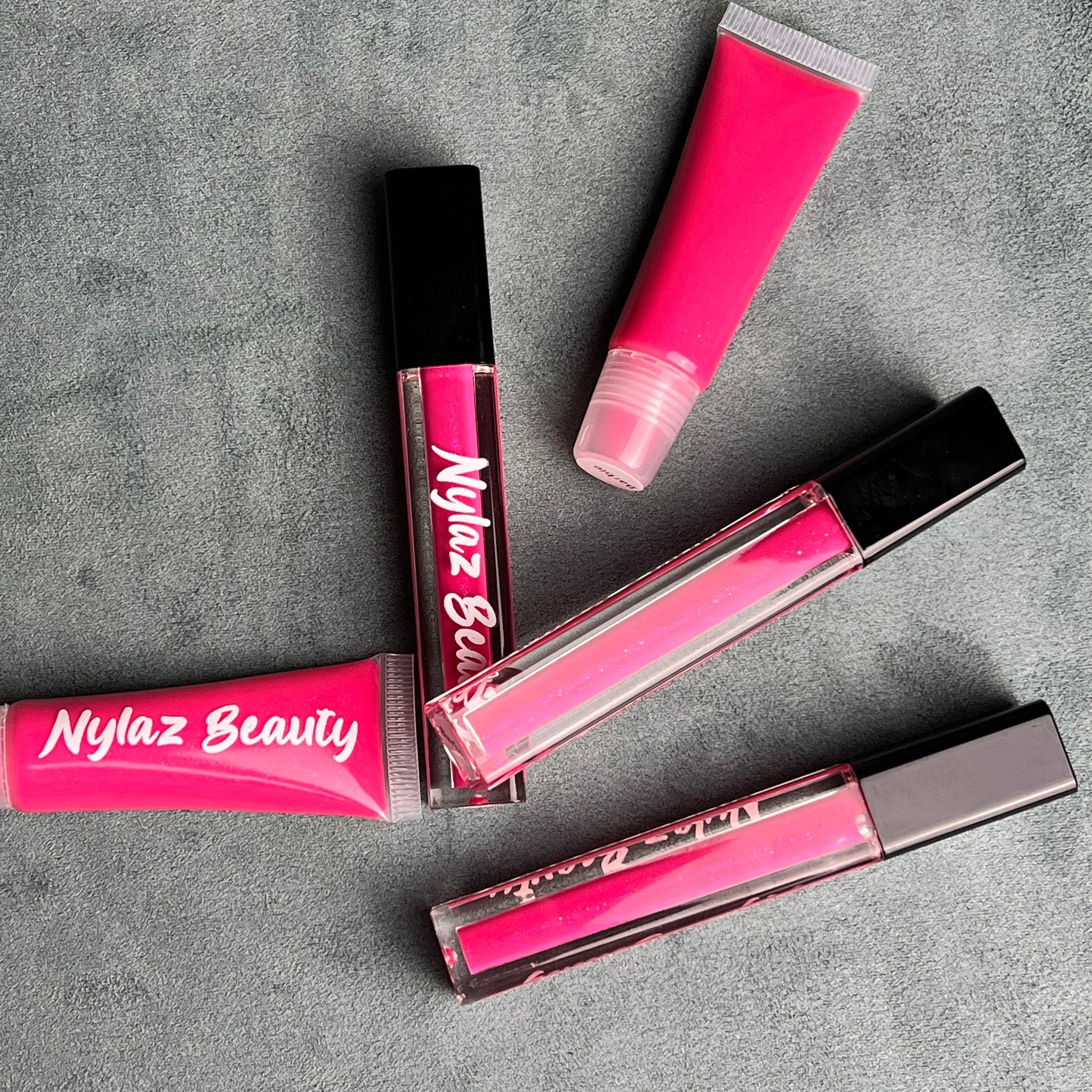 Lip gloss tubes in bright pink with black caps, "Nylaz Beauty" text visible on product packaging