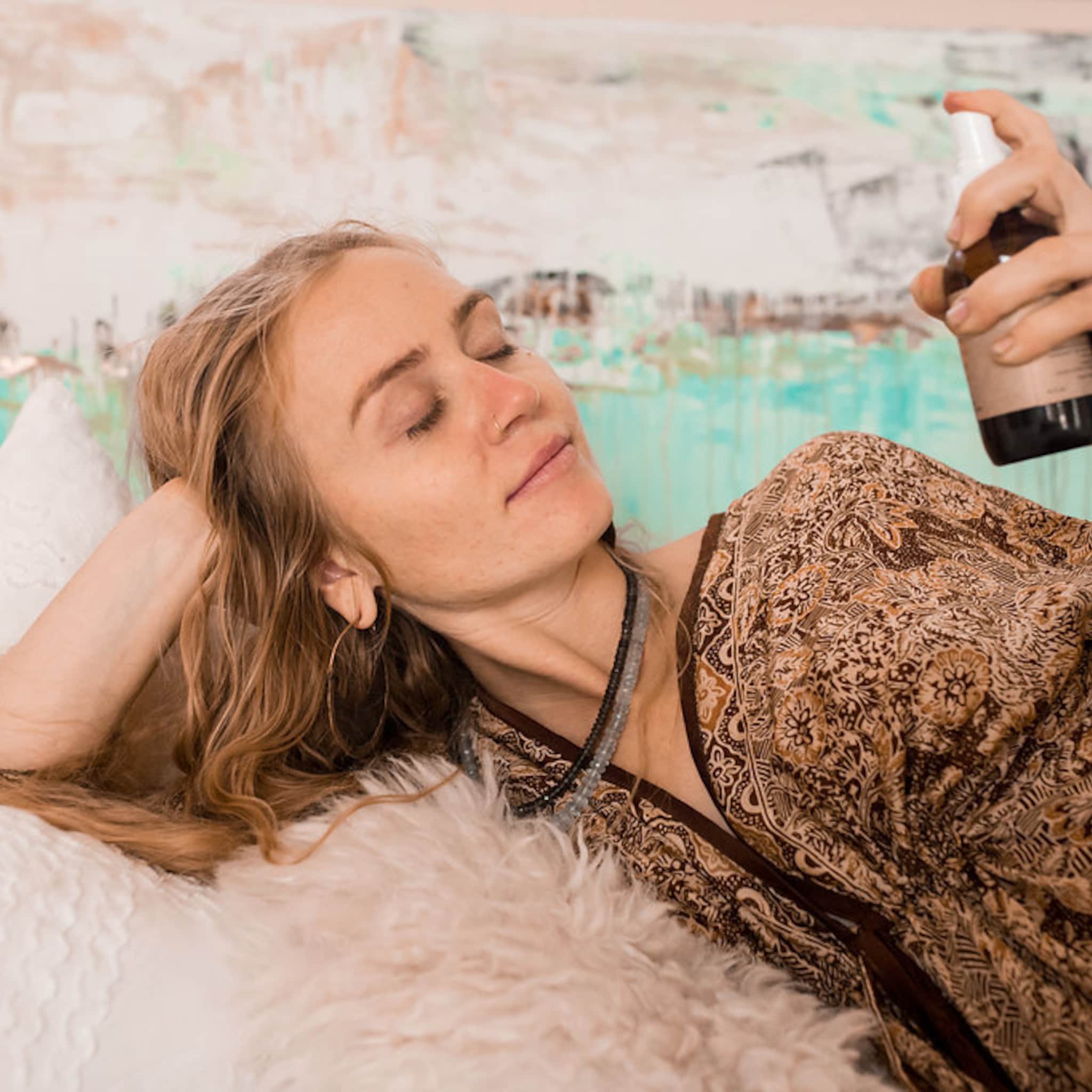 Woman lying down wearing brown patterned robe with spray bottle in hand