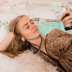Brown bottle being sprayed on woman, brown patterned robe, white fur blanket