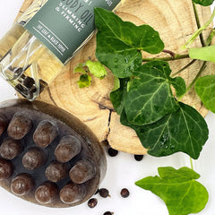 Body oil bottle with clear liquid, black peppercorns, and green label with text on a wooden surface