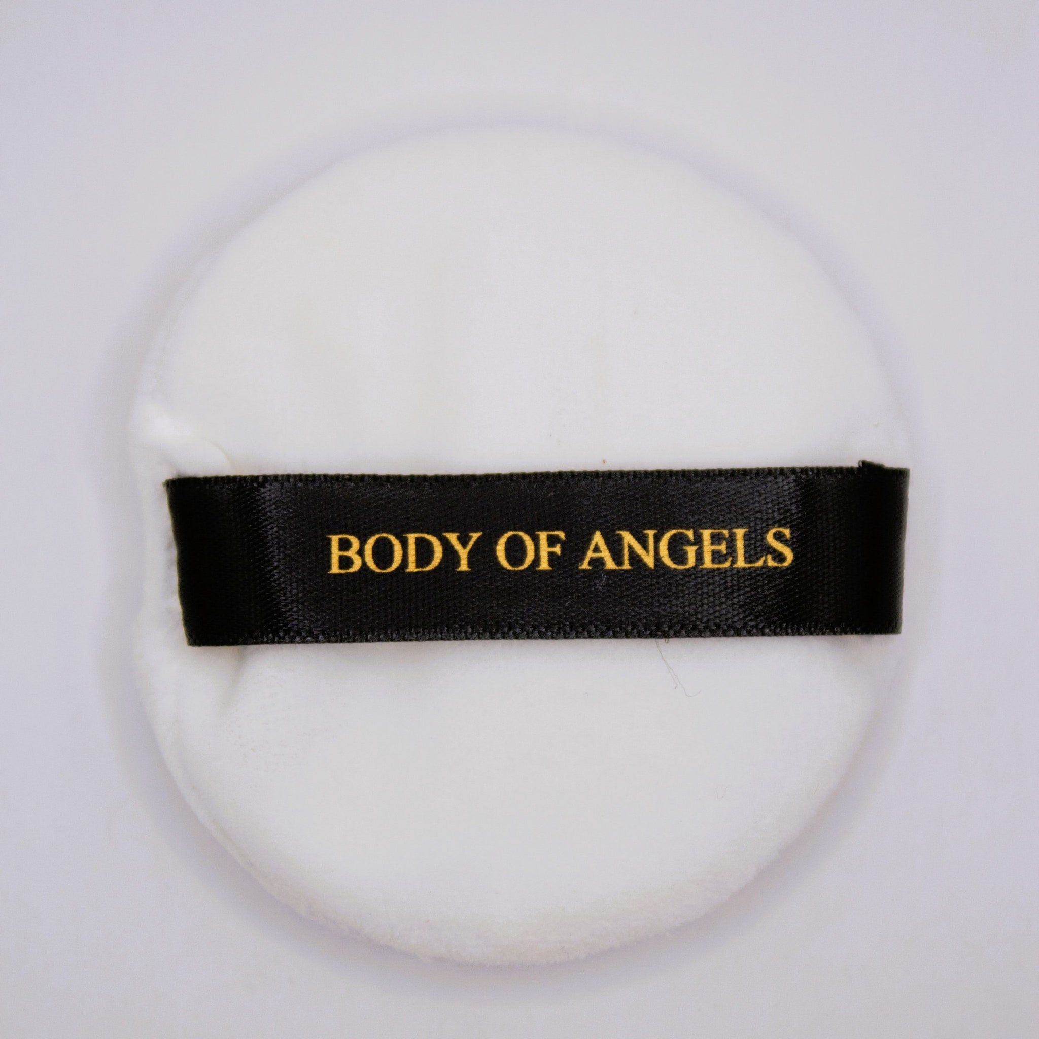 Powder puff with white material and black ribbon, "BODY OF ANGELS" text in gold