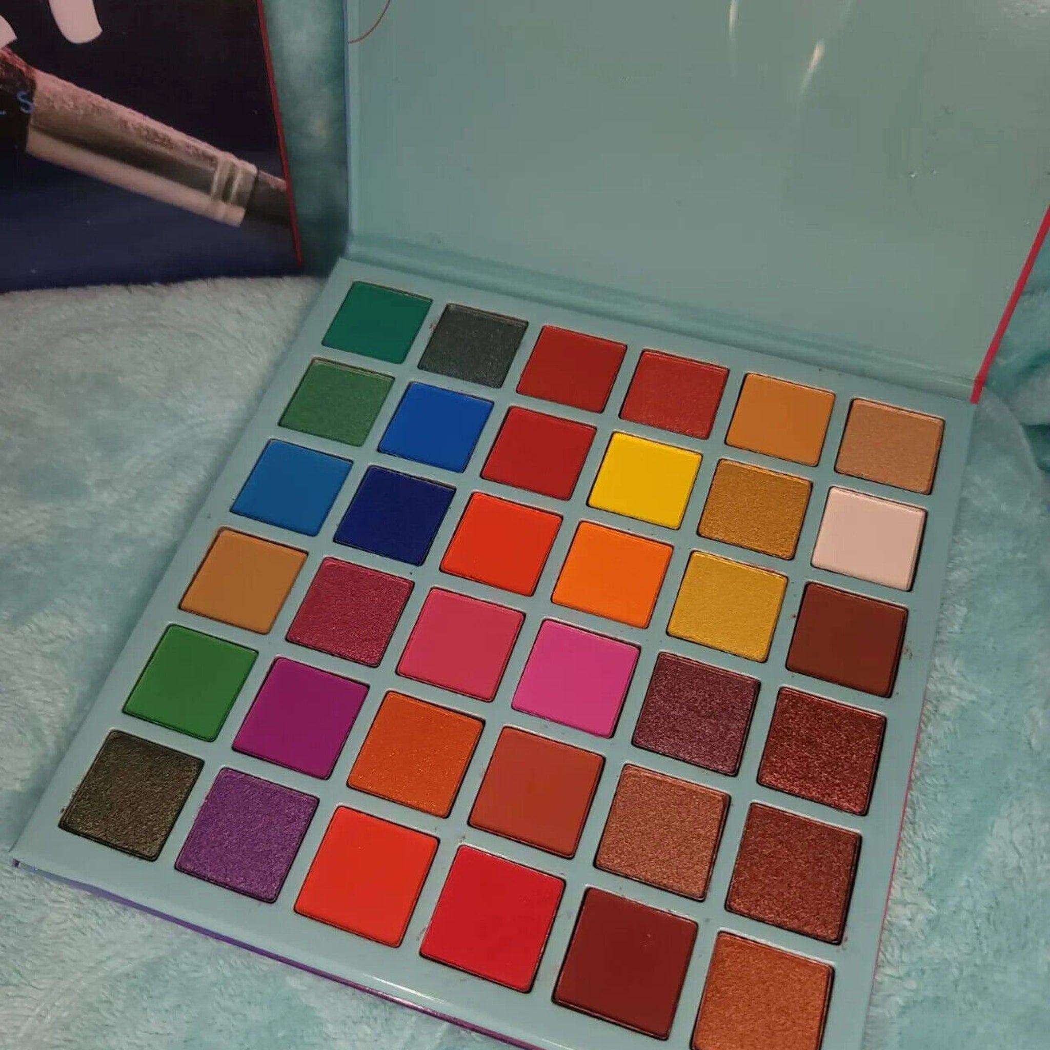 Open 36-color eyeshadow palette displaying vibrant matte and shimmer shades in rectangular pans with black case.