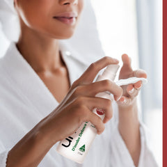 Spray bottle with white and clear bottle, green and red text, being sprayed onto a cotton pad.