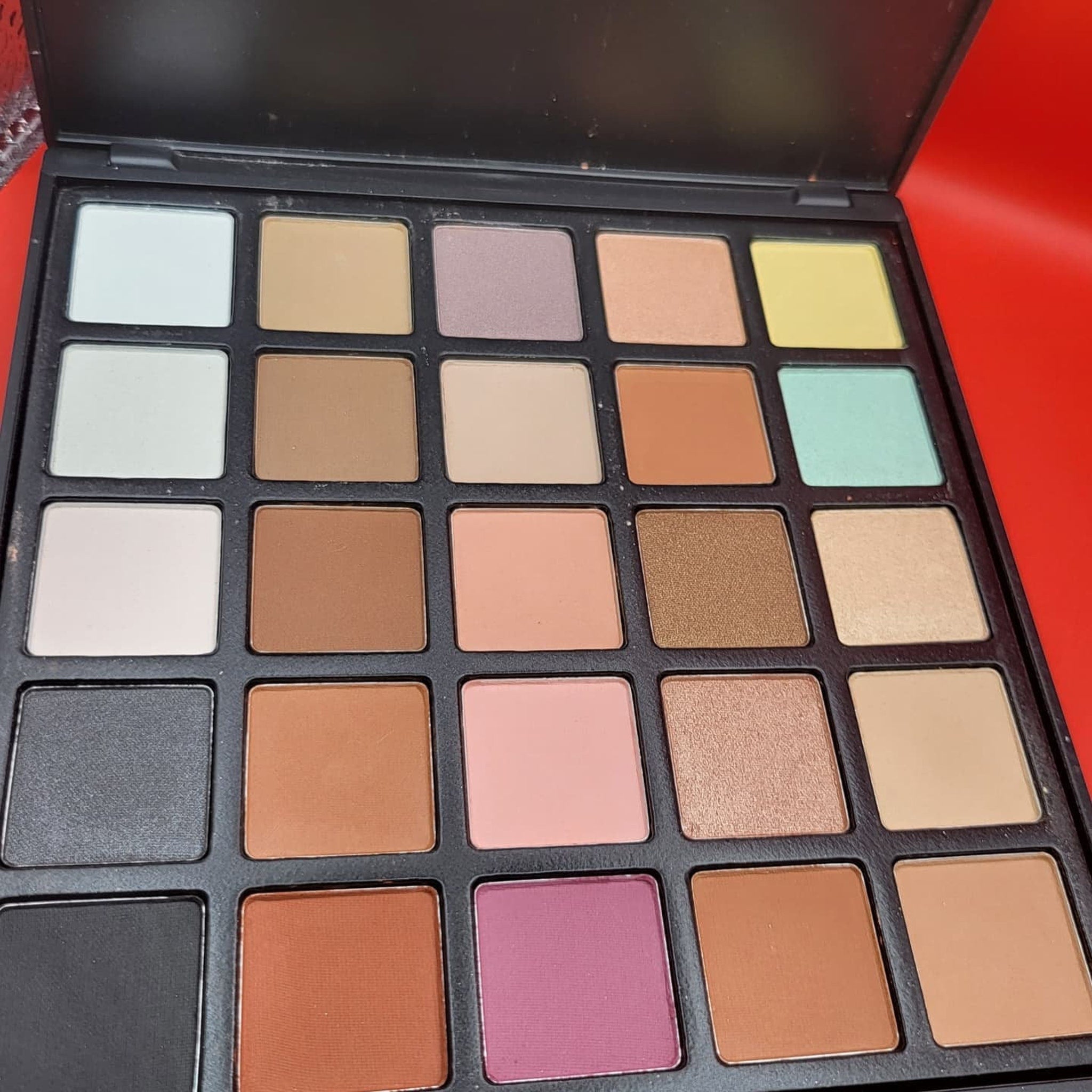 Close-up of shimmering bronze and plum eyeshadow pans in a 25-color palette with mirrored compact