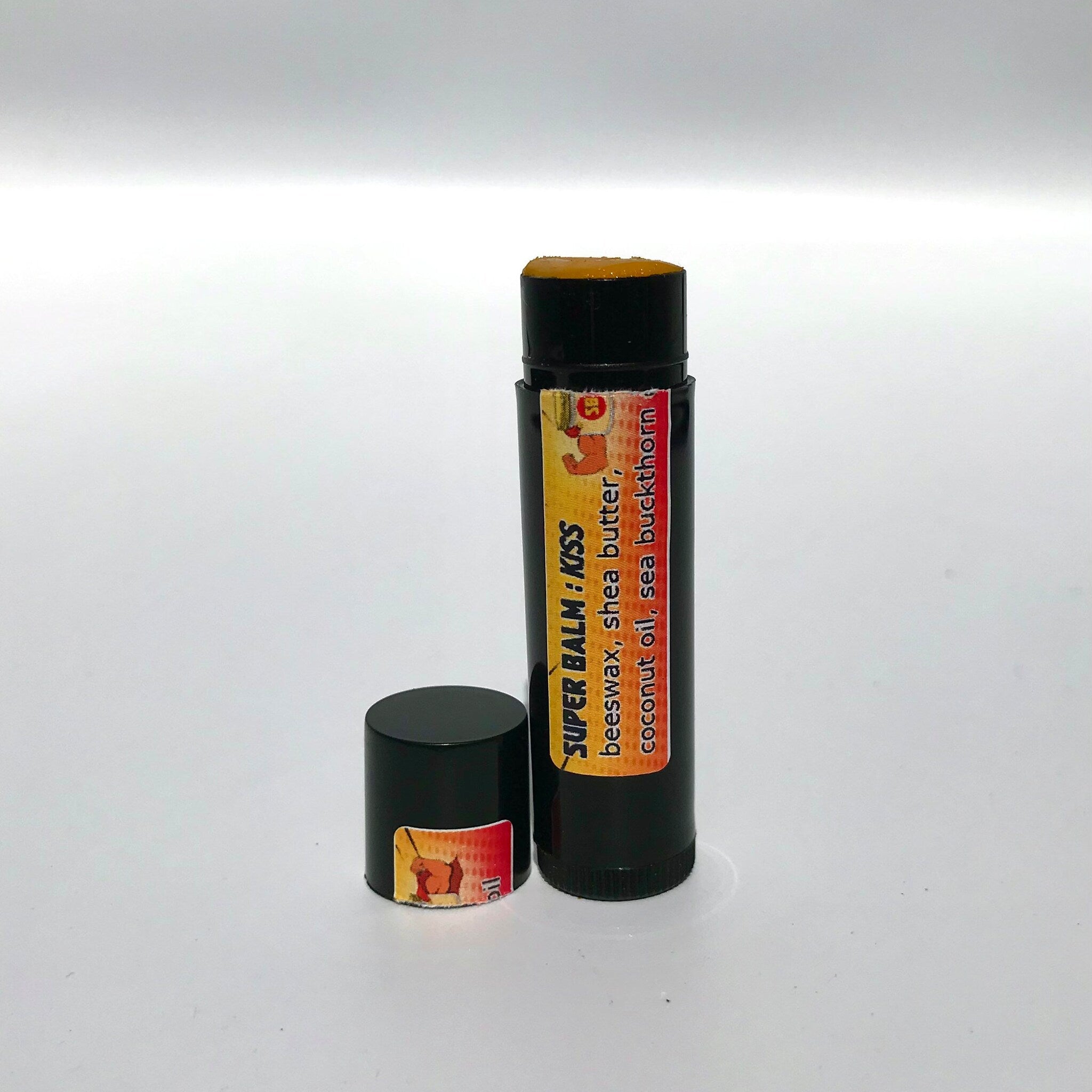 Lip balm stick with black tube, orange balm, and "SUPER BALM: KISS" label visible