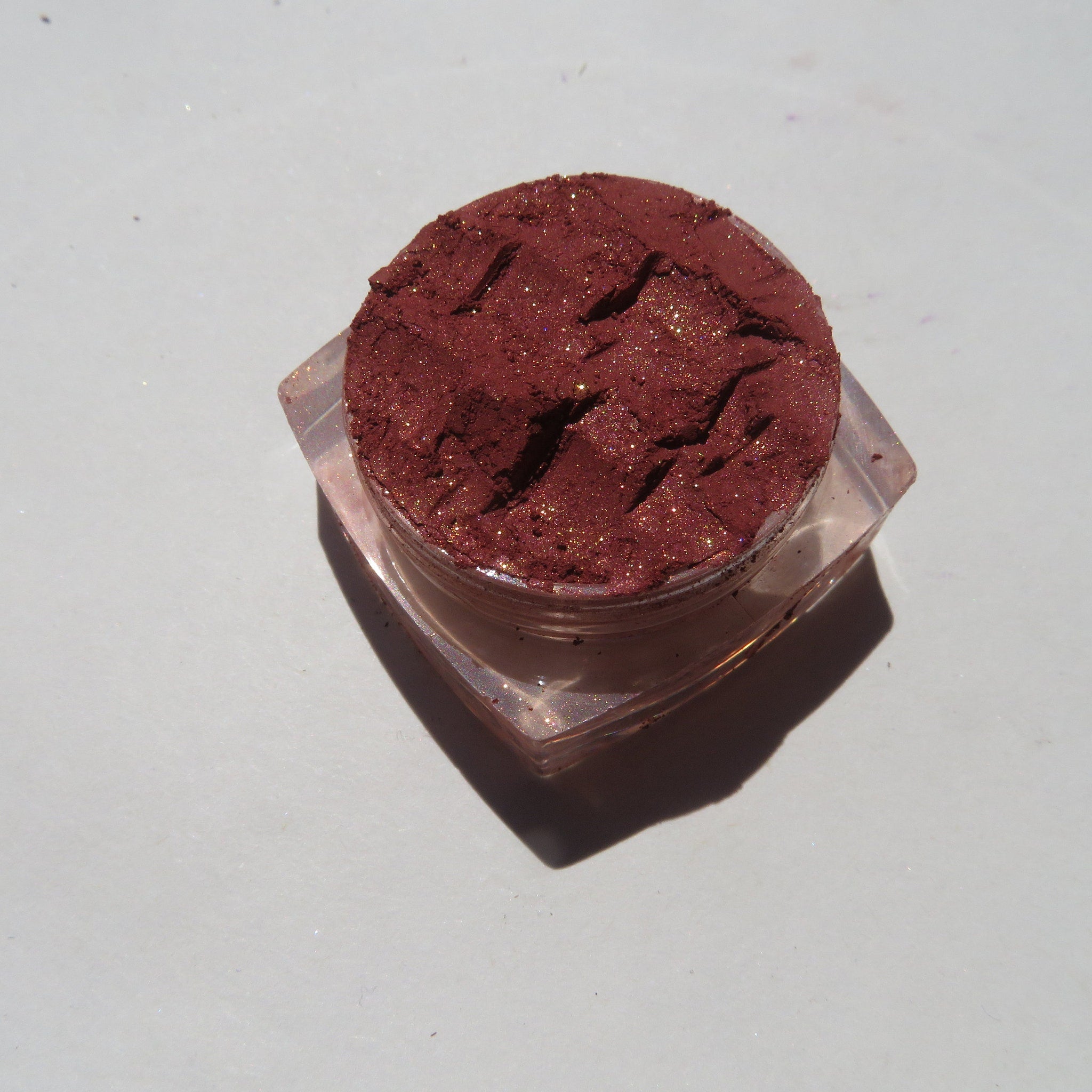 Side view of loose brick red orange shimmer mineral eyeshadow powder spilling from jar