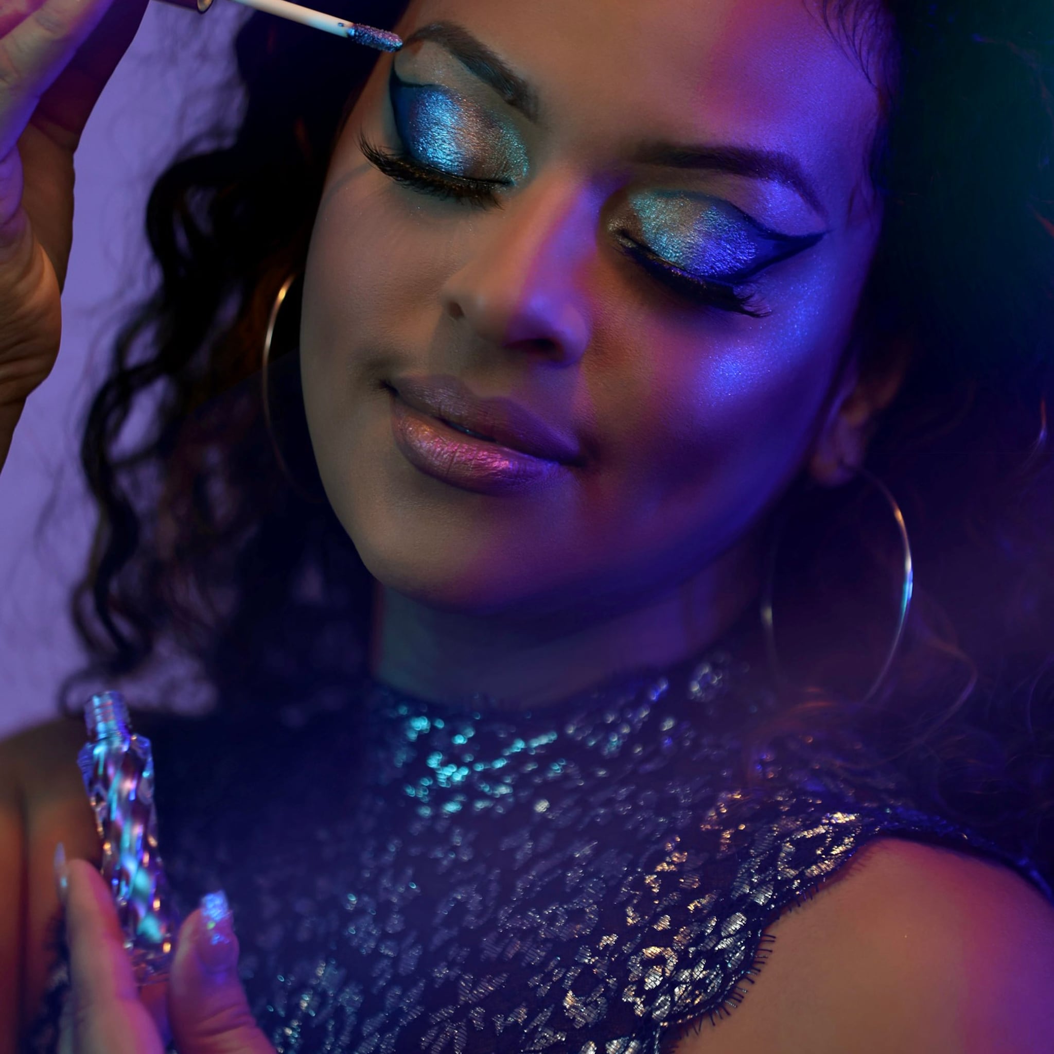 Eyeshadow makeup with blue and silver shimmer, black eyeliner, and a woman applying it