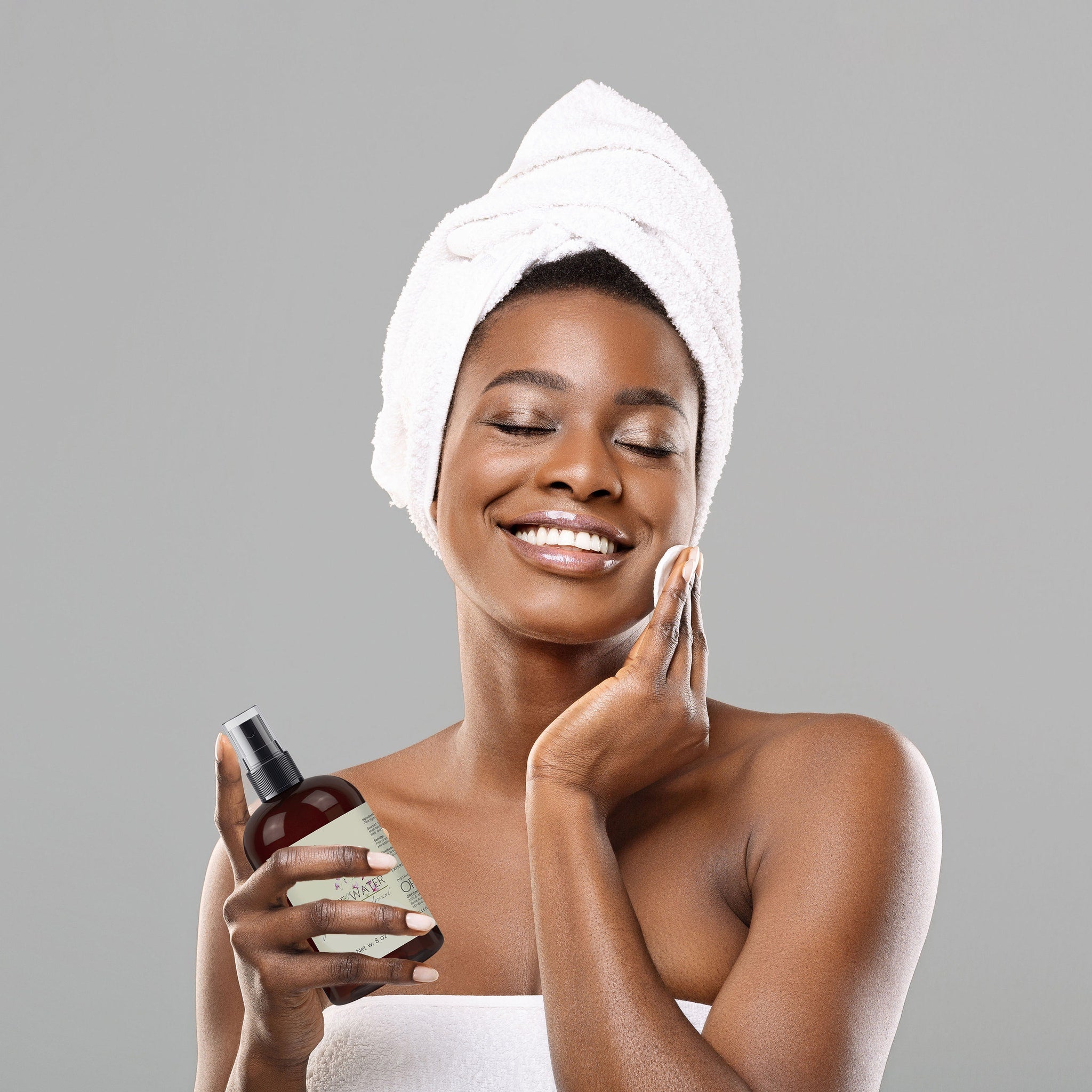 Facial toner bottle brown glass with black spray top, held by woman with white towel on head