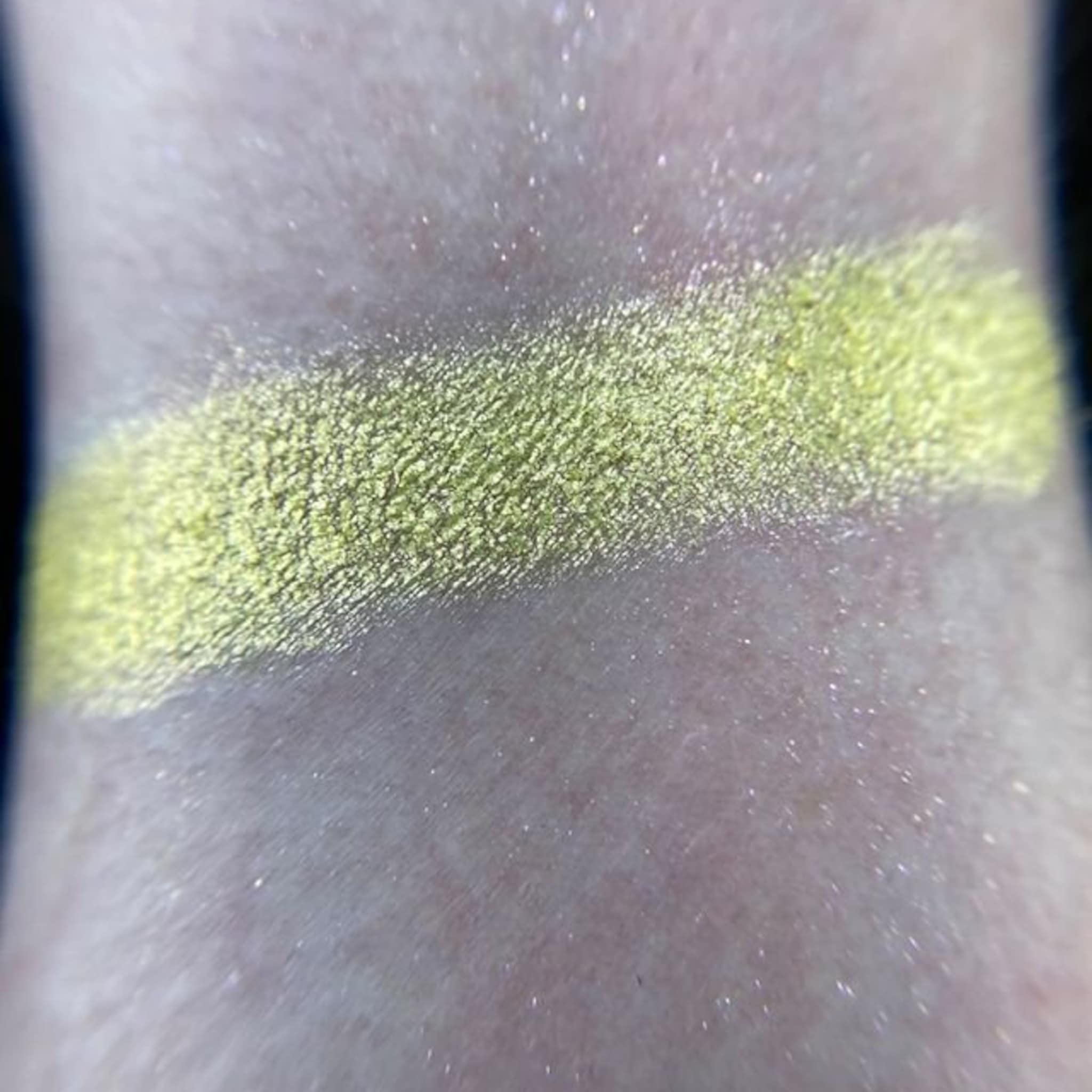 Eyeshadow swatch with lime green shimmer on skin, showing texture and color
