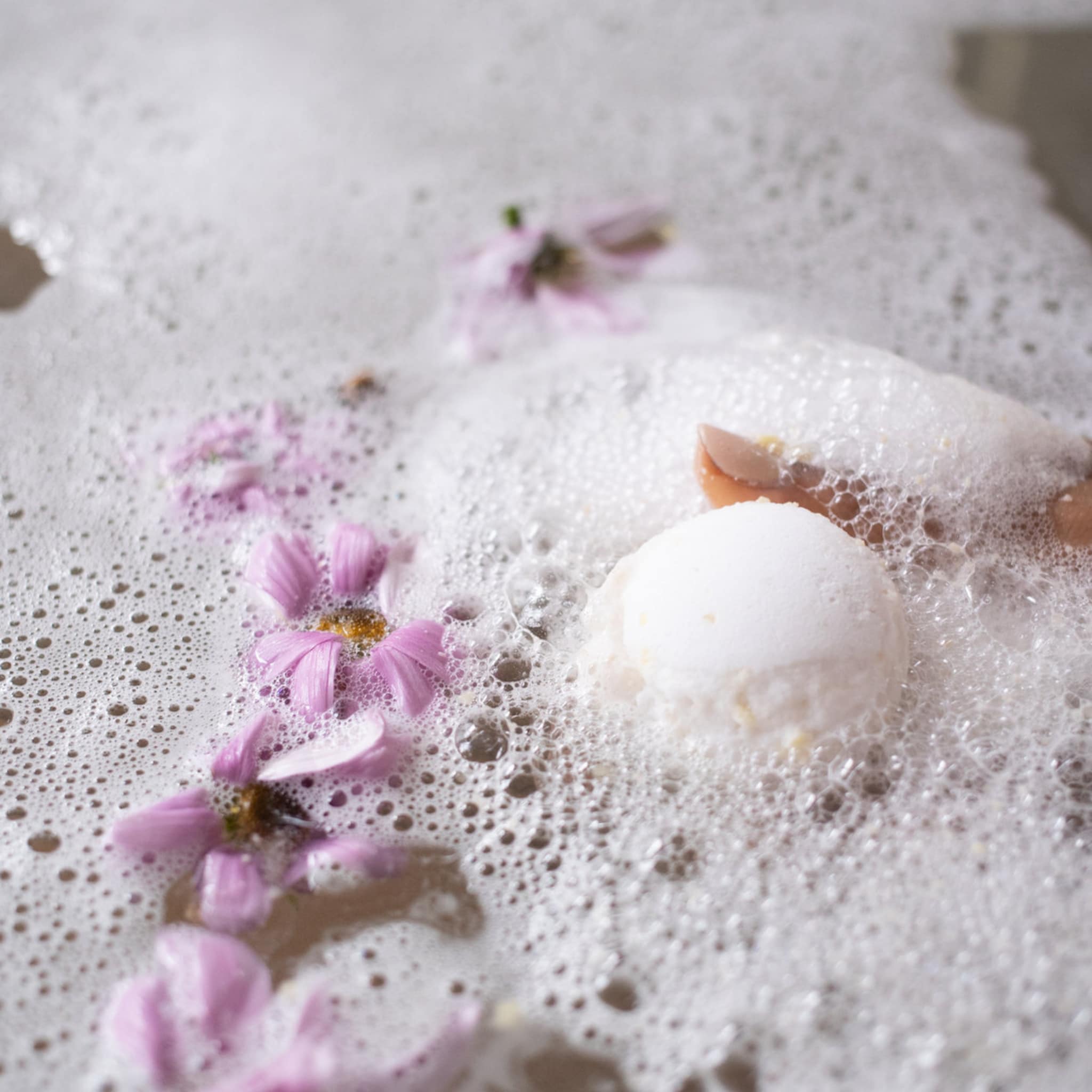 Bath bomb in white with pink flower petals and bubbles, in bath water