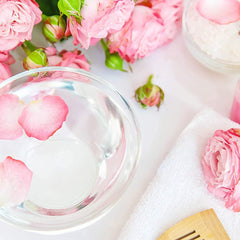 Pink rose petals in clear bowl with white towel and wooden comb, spa setting
