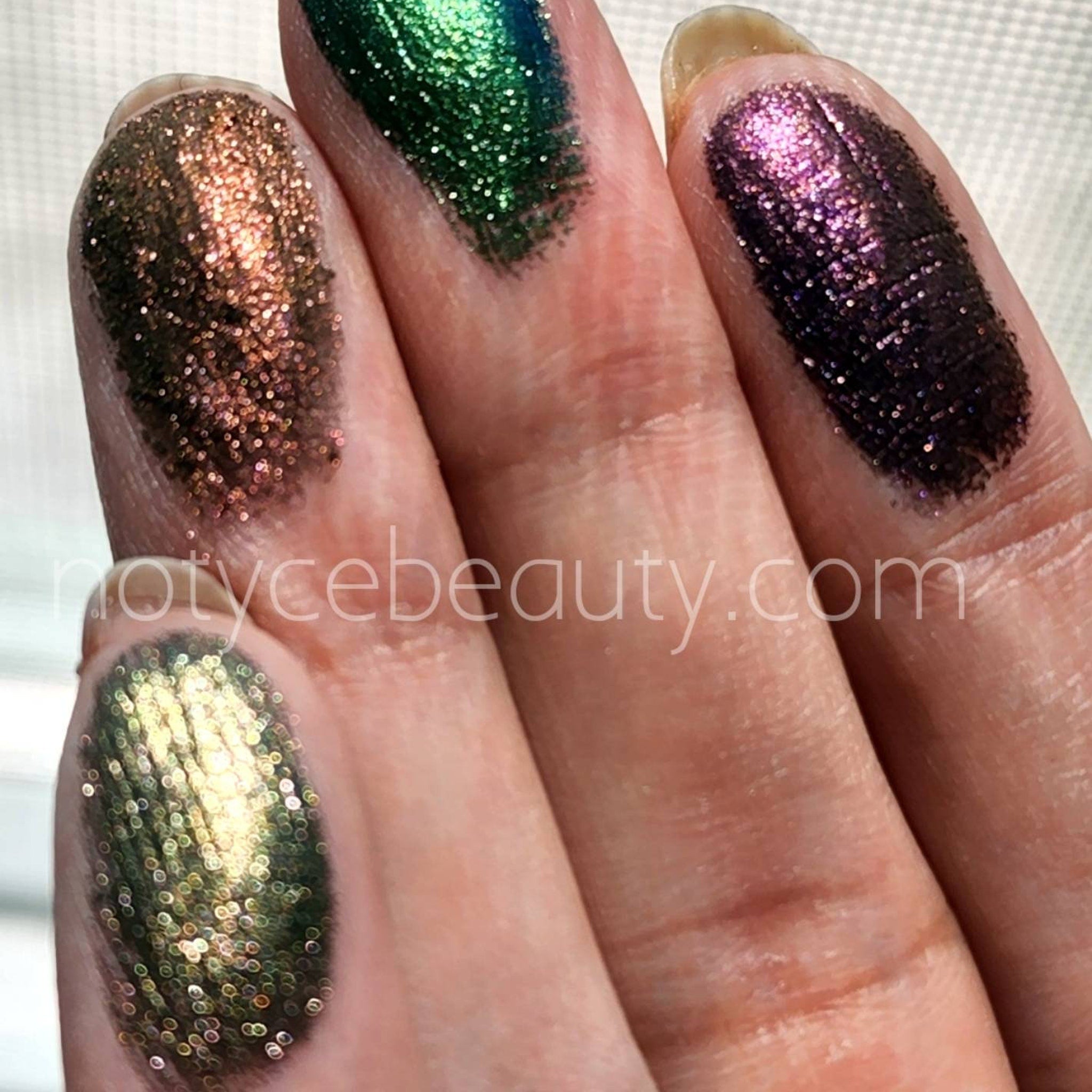Glitter eyeshadow swatches in bronze, green, and purple shades on fingertips, notycebeauty.com text visible