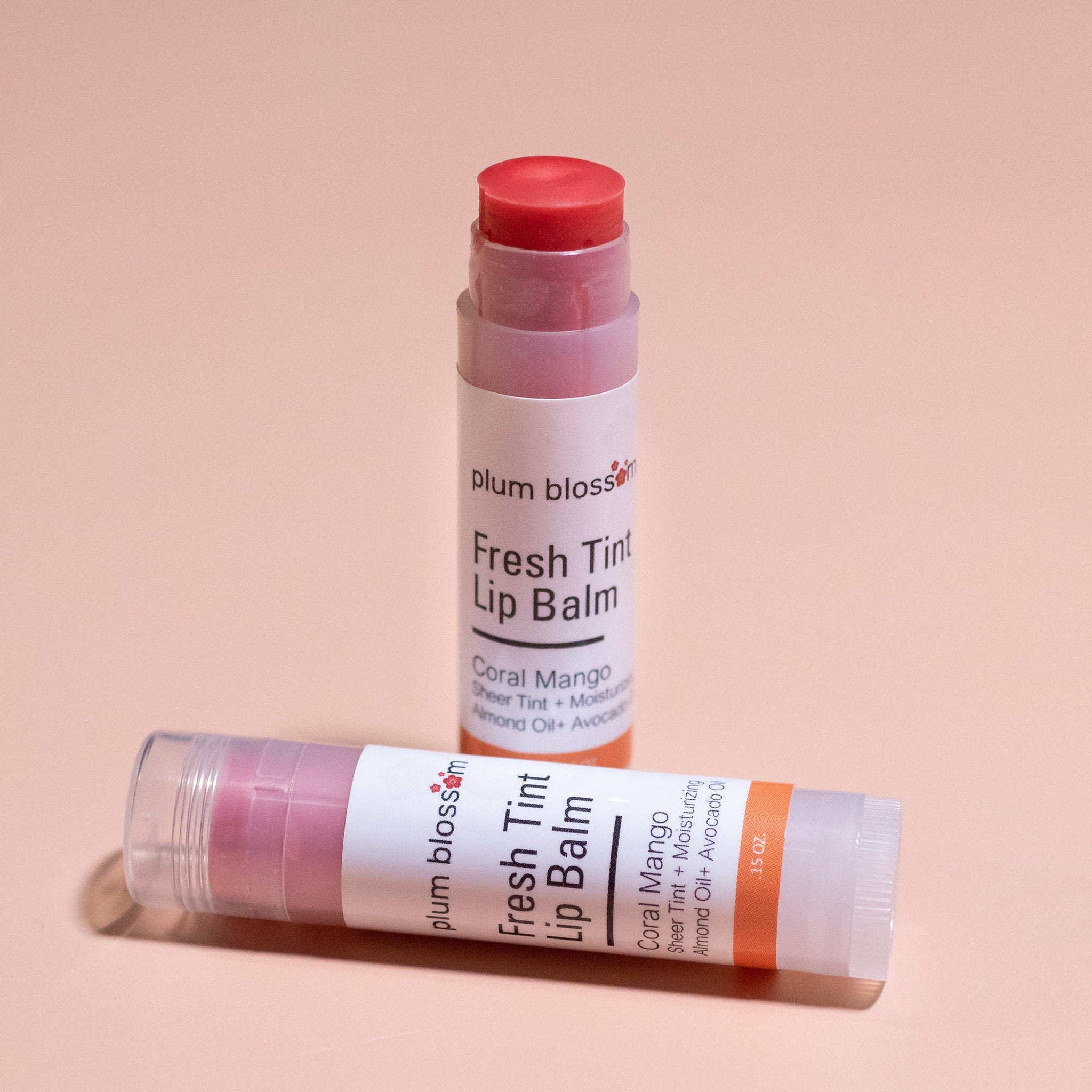 Lip balm tubes with coral and pink tints, white label, plum blossom brand name visible