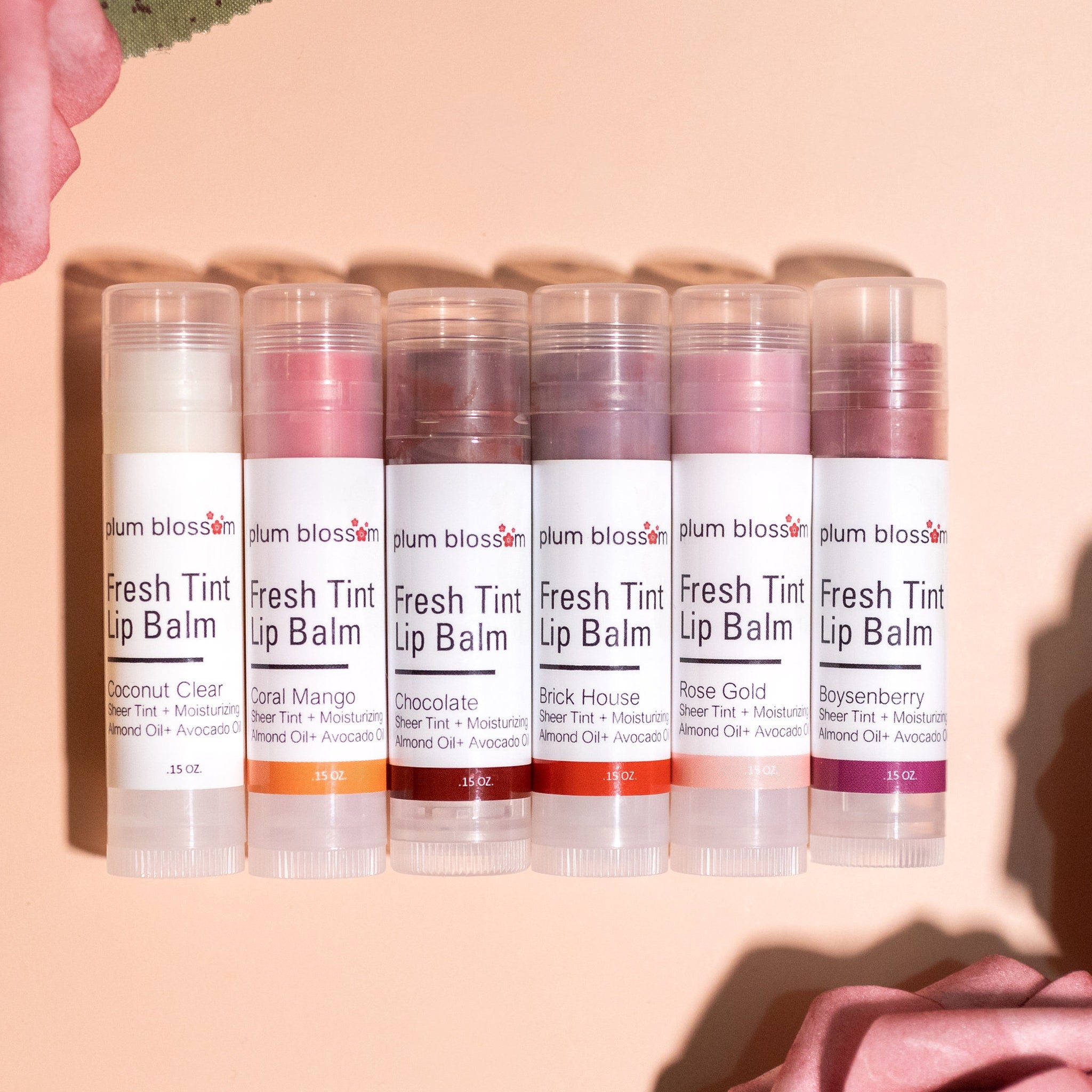 Lip balms in various colors, clear plastic tubes, Plum Blossom Apothecary brand name visible