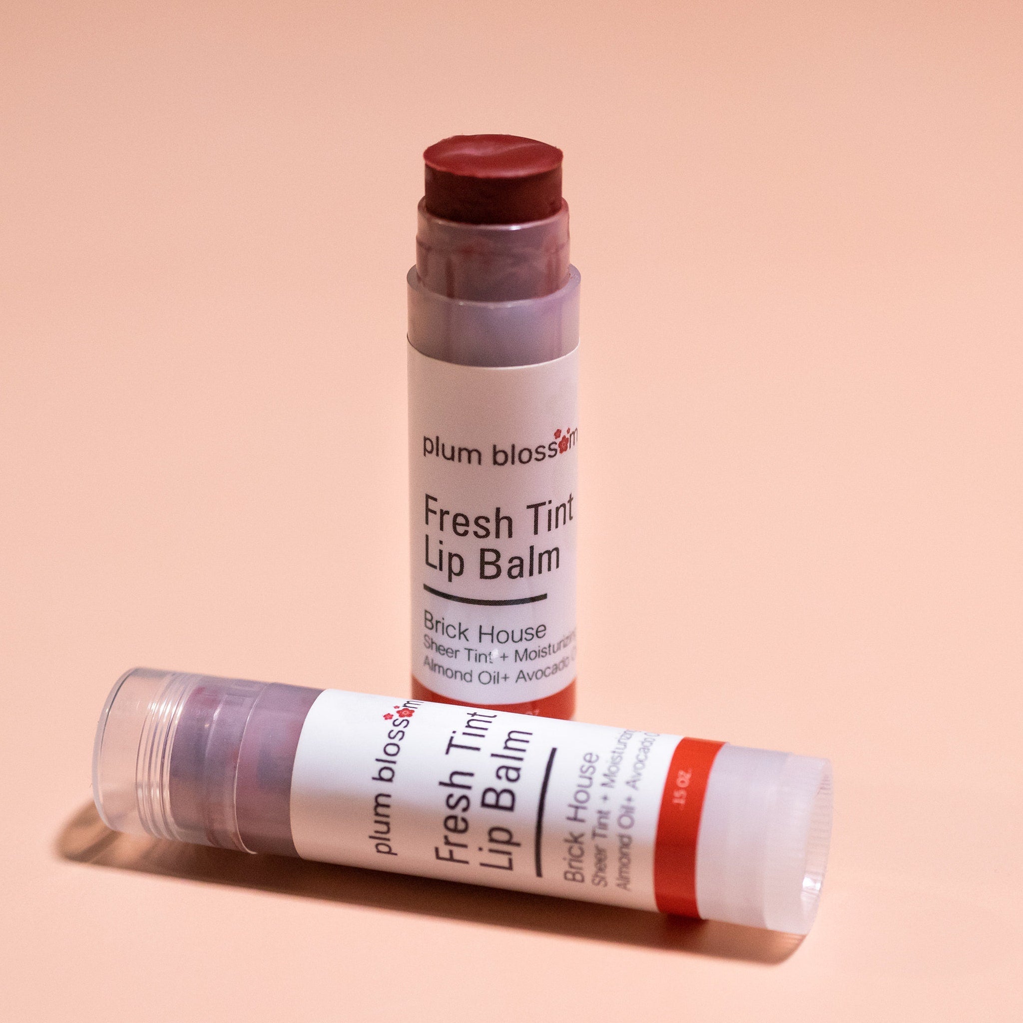 Lip balm tubes with red and white labels, dark red balm, and clear plastic cap on peach background