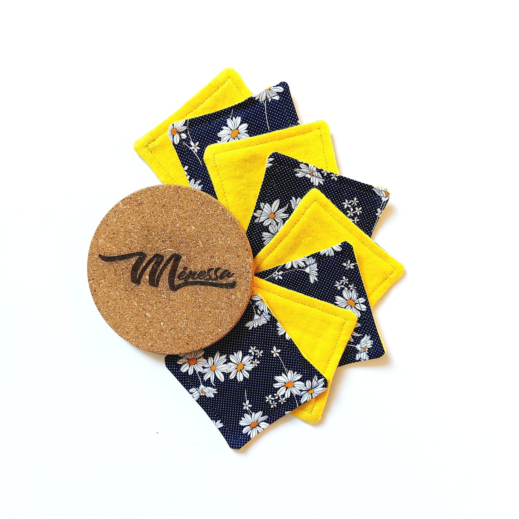 Coasters with yellow and floral fabric, cork coaster with "Menessa" text, top view
