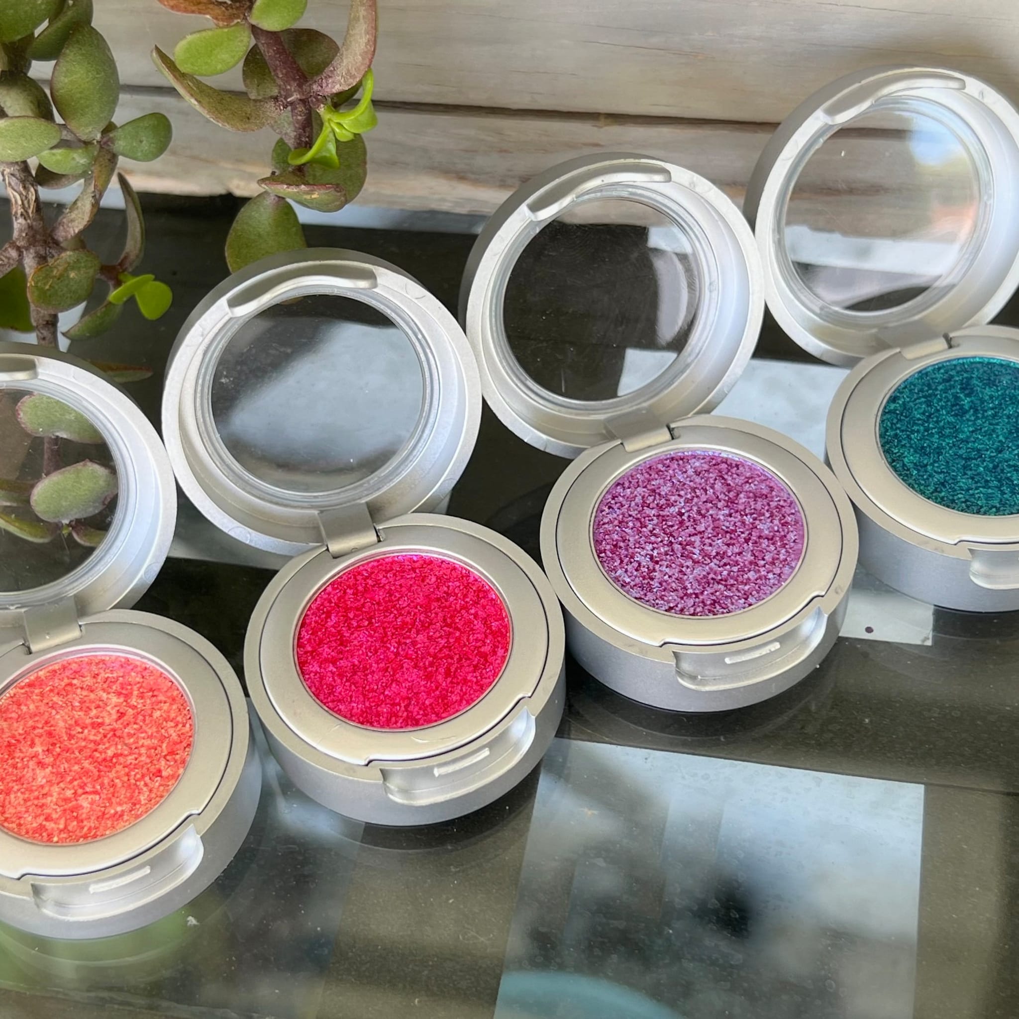 Eyeshadow compacts with silver casing, various colored textured powders, and clear lids