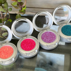 Eyeshadow compacts with silver casing, various colored textured powders, and clear lids