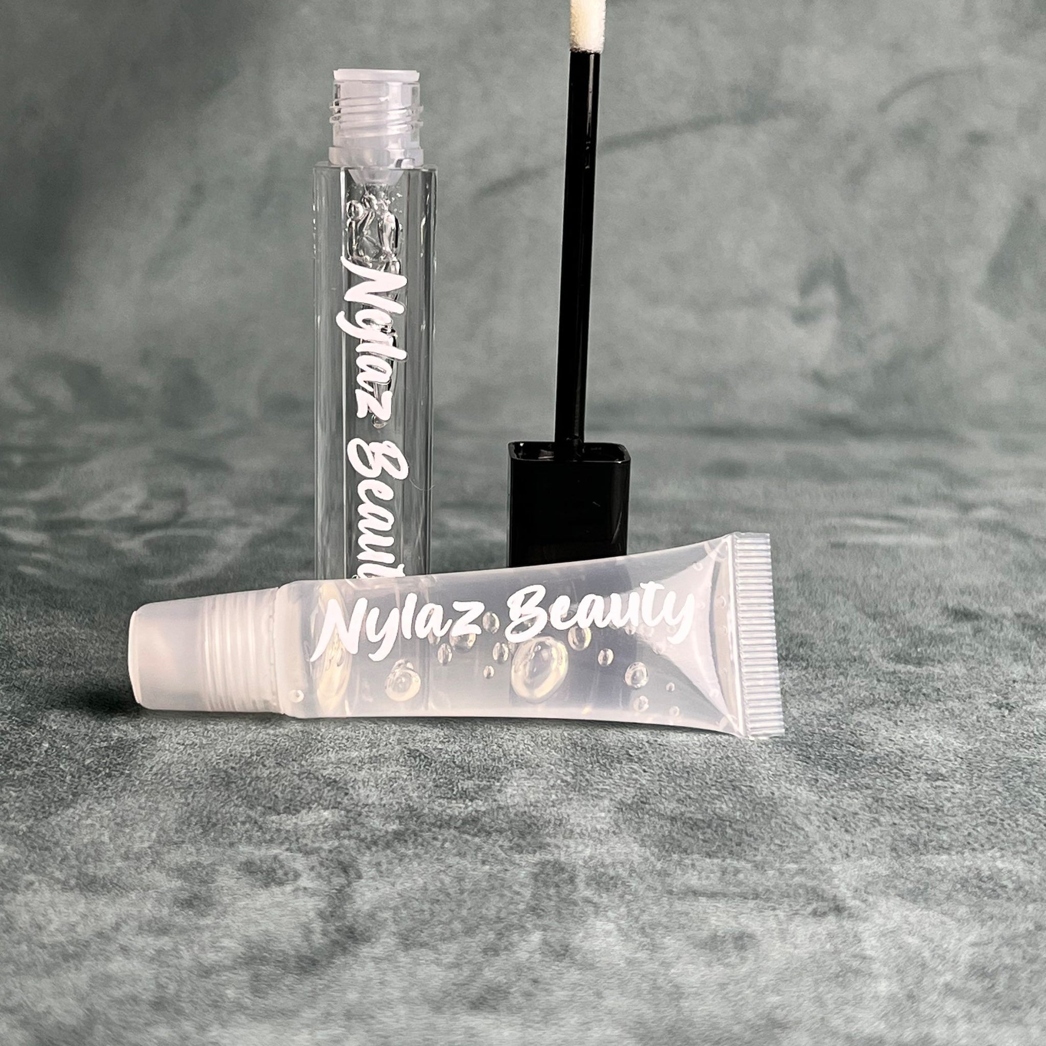 Lip gloss tubes, clear liquid, white text, black applicator, Nyiaz Beauty brand