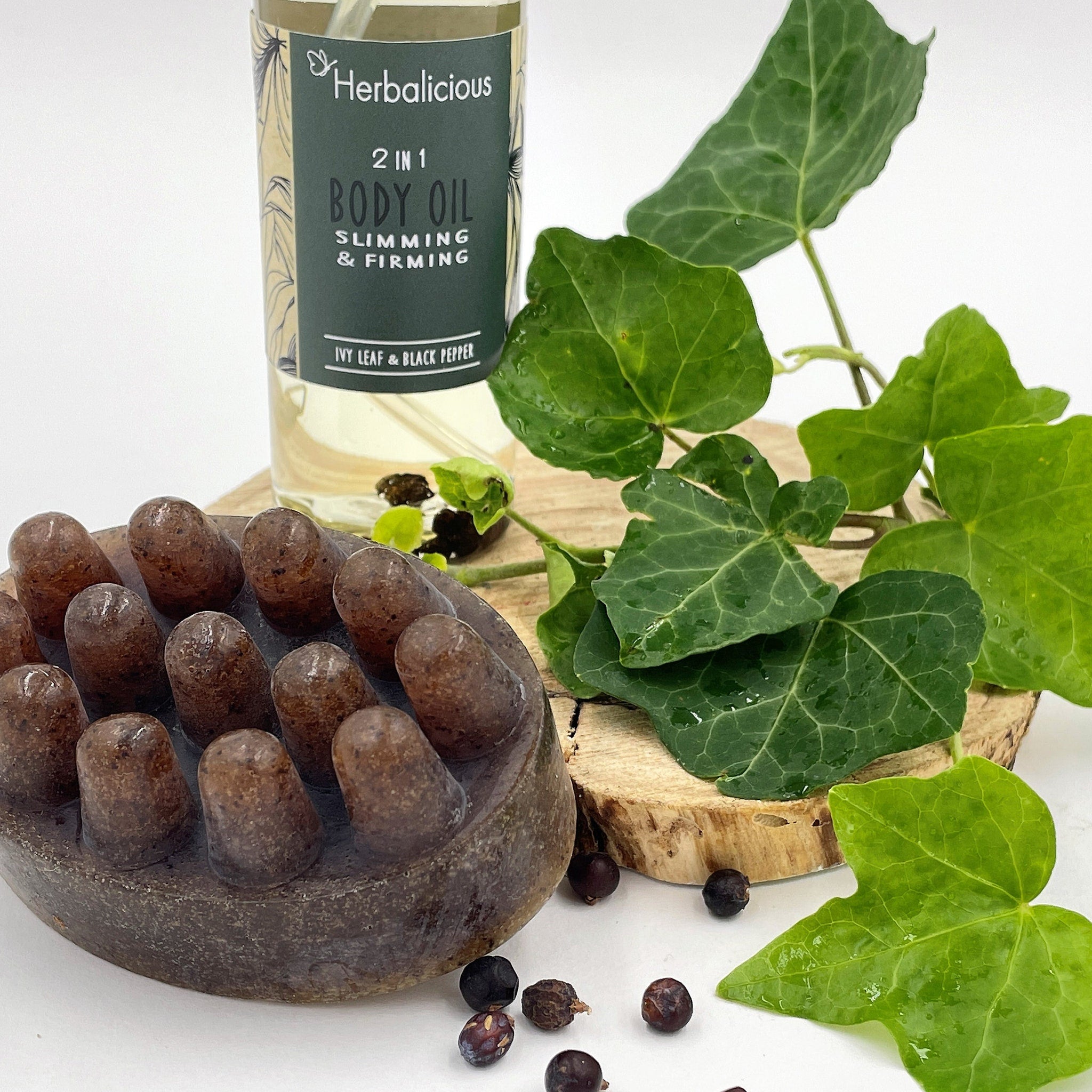 Body oil bottle, clear liquid, green and white label, Herbalicious brand, with green leaves and brown soap
