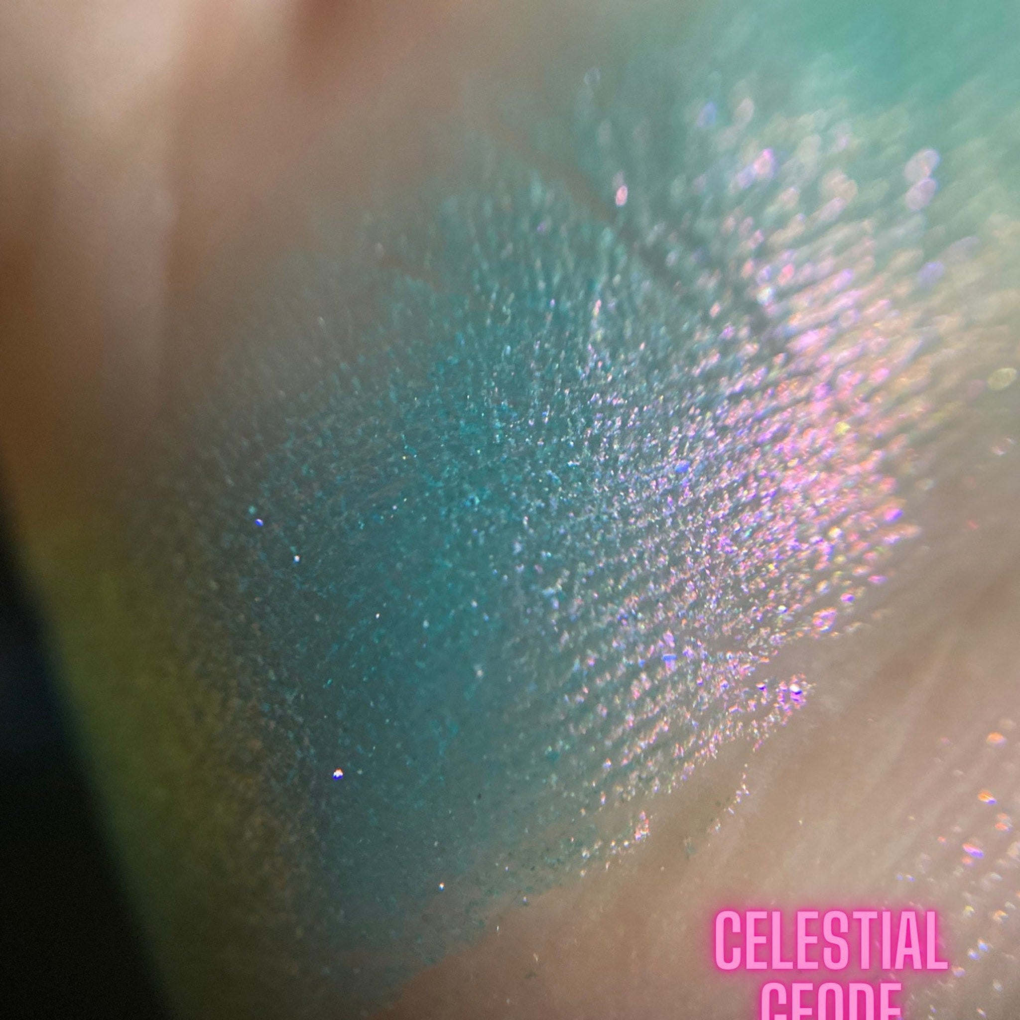 Eyeshadow swatch with teal and pink shimmer, Celestial Geode text visible on skin
