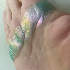 Makeup swatch with iridescent green and silver shimmer on skin, showing texture and color variations