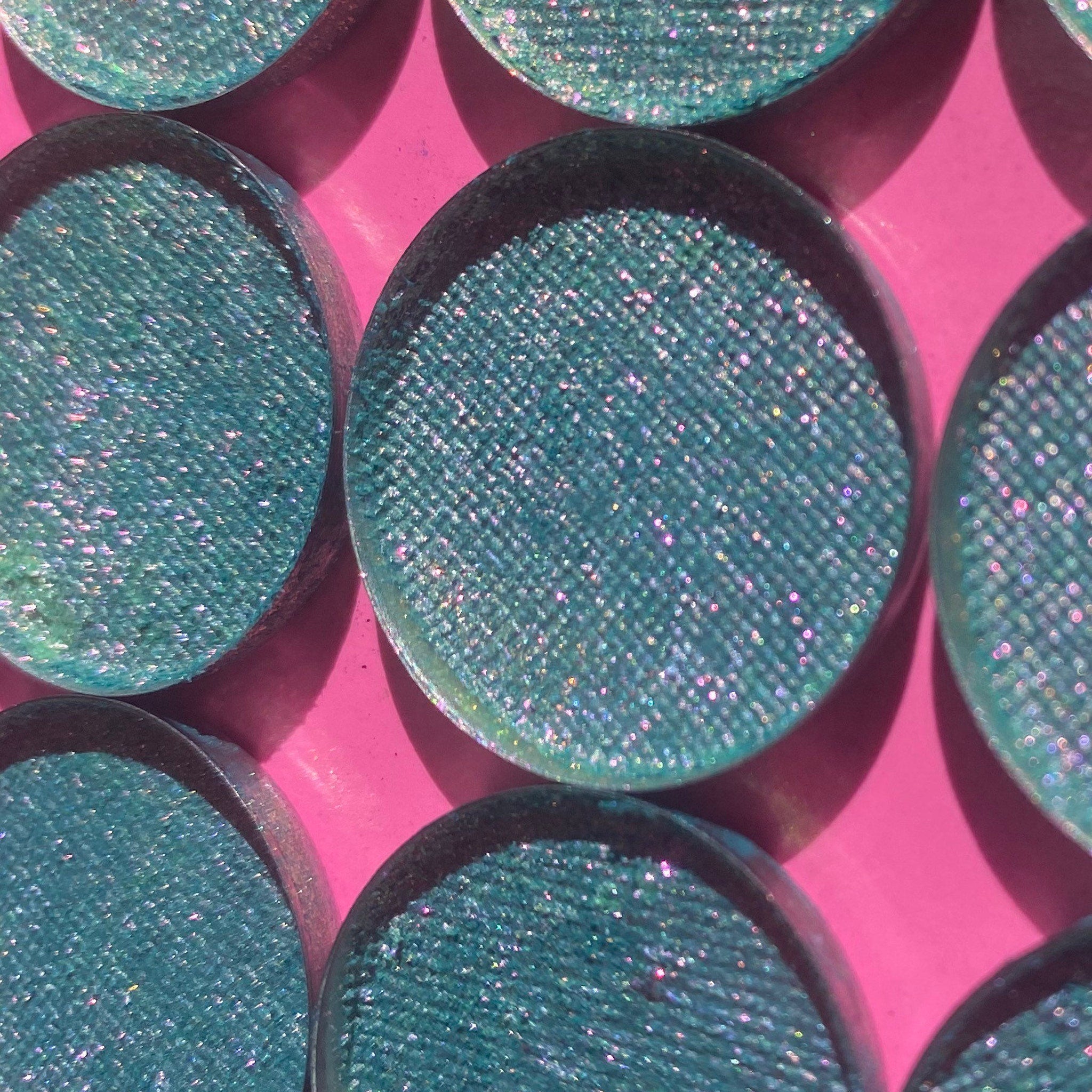 Eyeshadow pans, teal glitter, round shape, on pink background