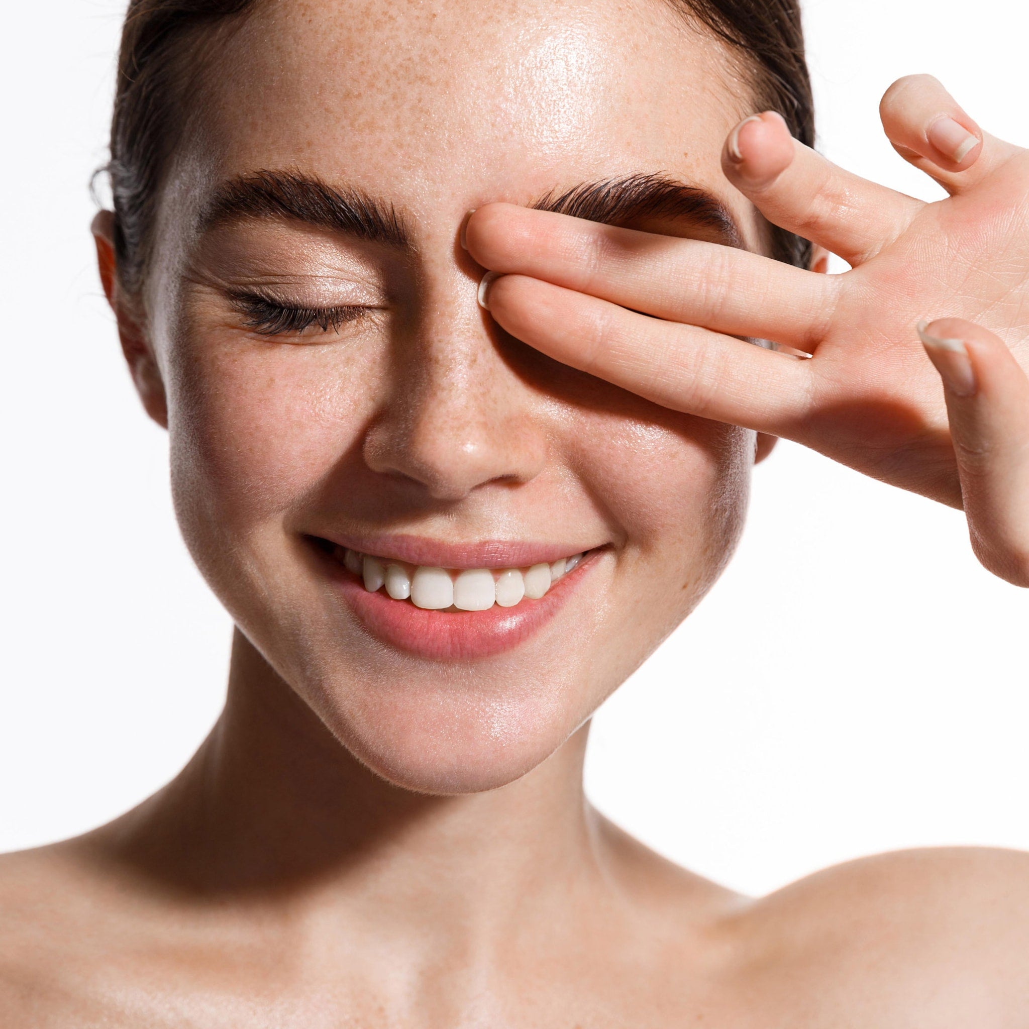 Smiling woman with closed eyes and hand covering face, freckled skin, white background
