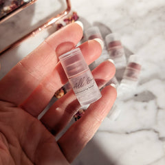 Tinted lip balm in clear plastic tube, held in hand with "All Day" text visible
