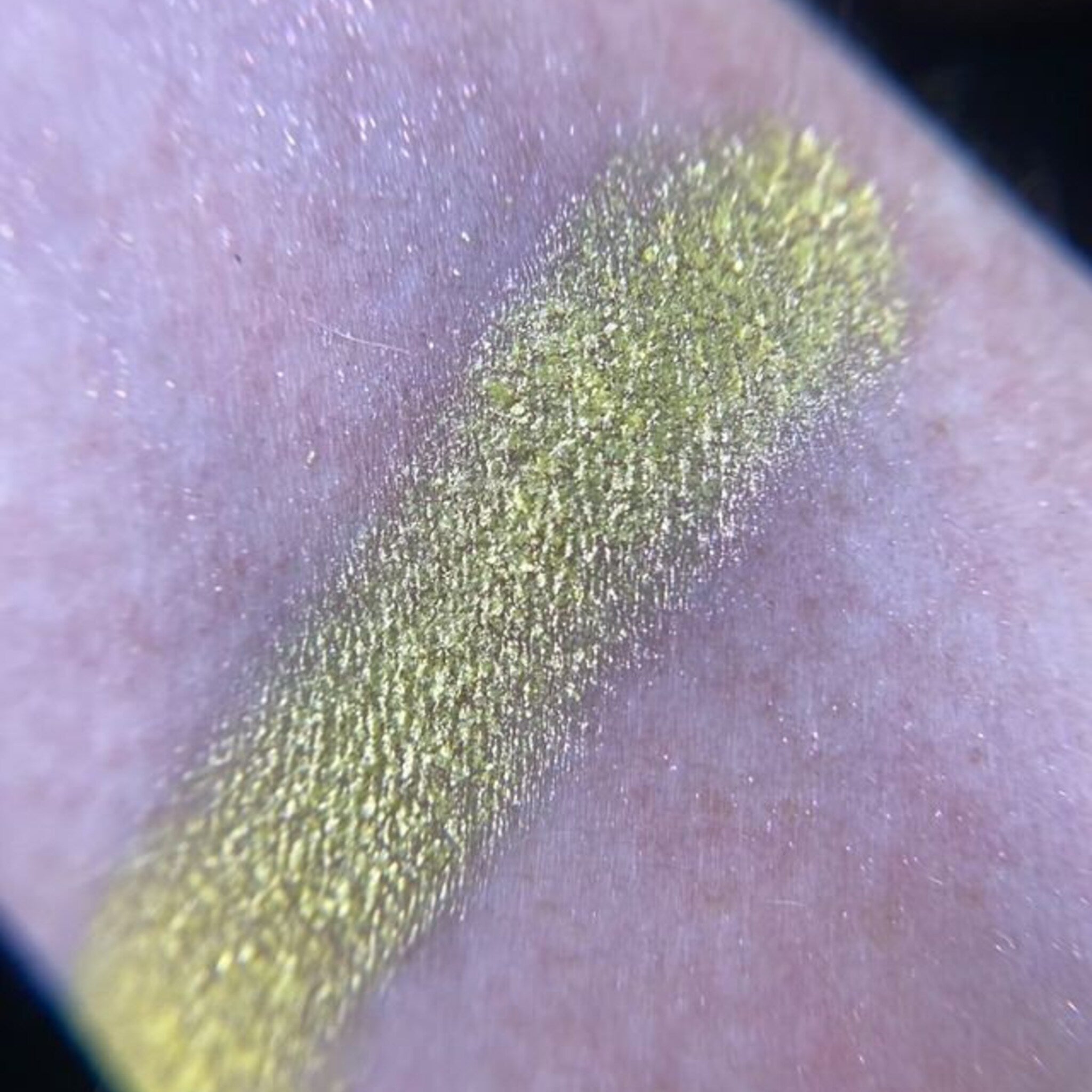 Eyeshadow swatch, yellow-green shimmer, textured application on skin, close-up view