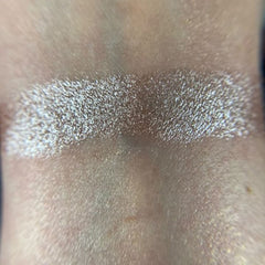 Woman applying shimmery champagne eye shadow with fingertip to eyelid for a glowing makeup look