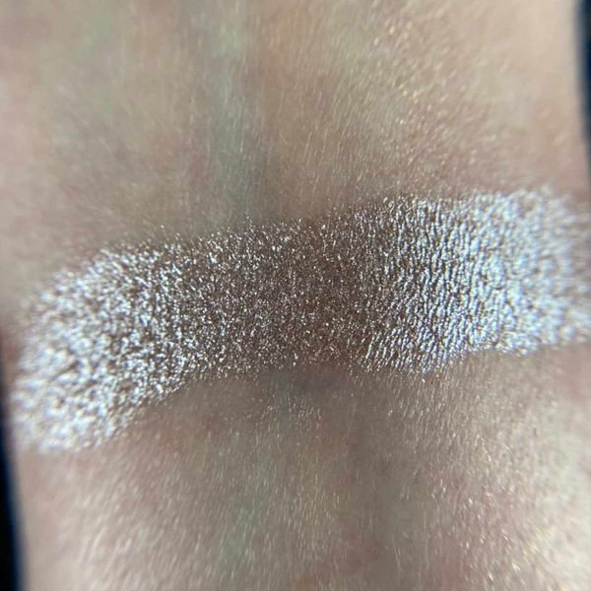 Square compact of shimmery champagne eye shadow with gold detailing and clear lid showcasing product.