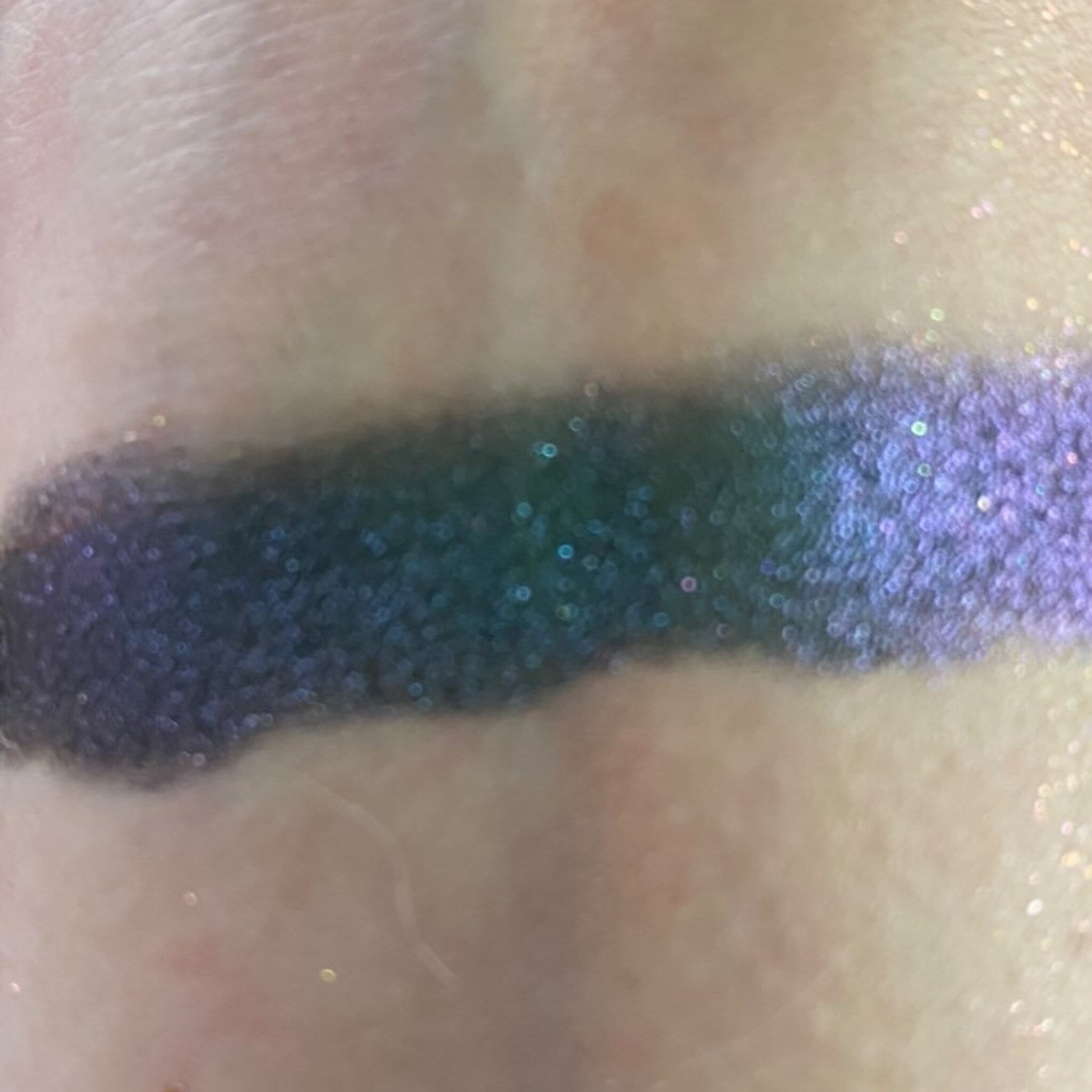 Close-up of fingertips applying shimmery taupe eye shadow to eyelid with soft blending brush