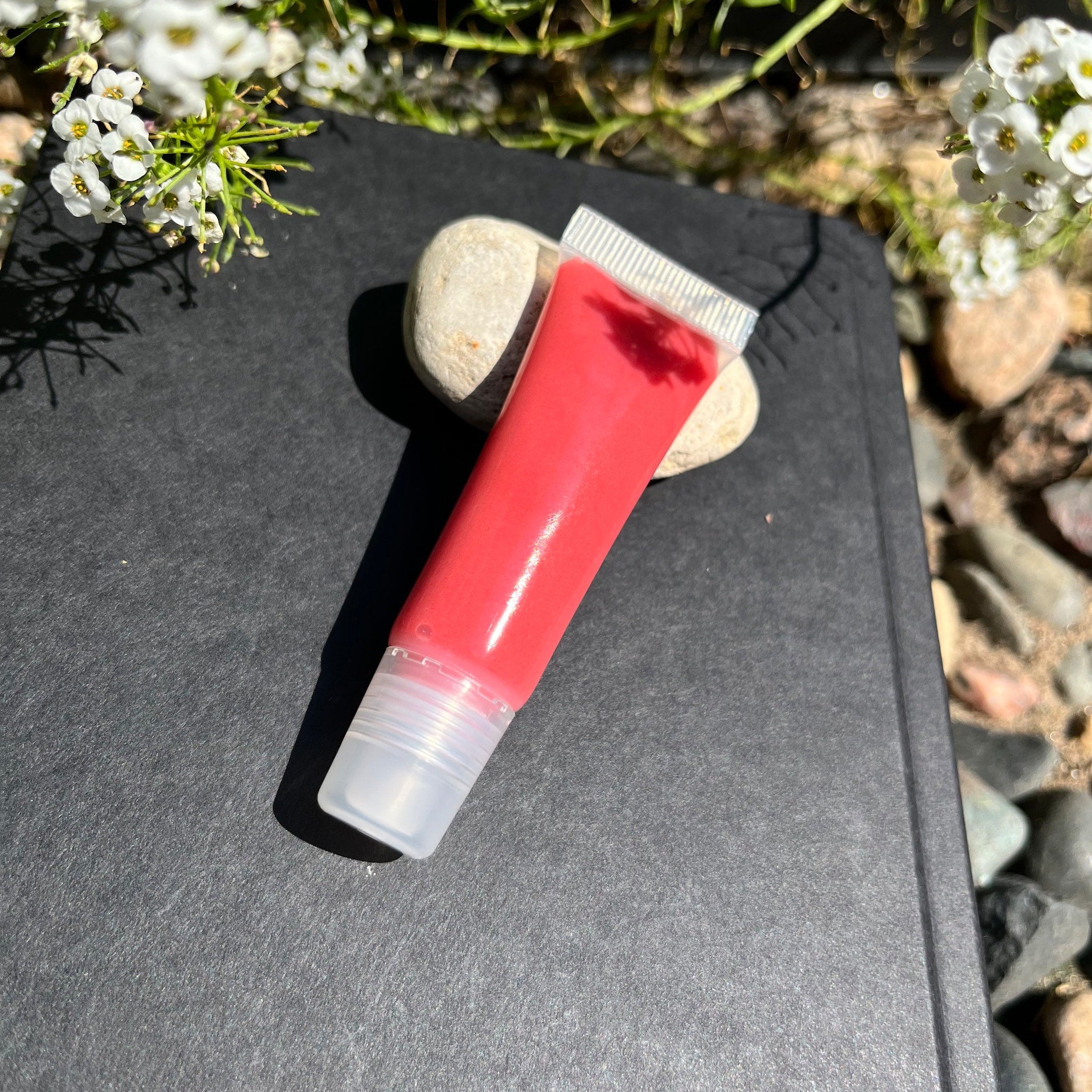 Lip gloss tube with red gloss, clear applicator, and white packaging on black surface